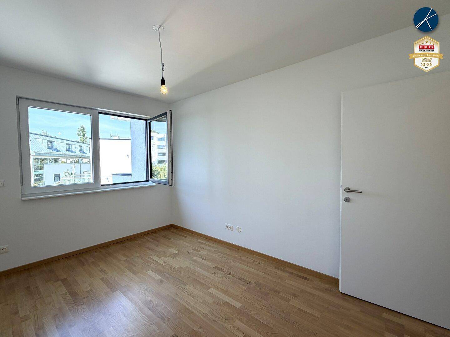 Helles Schlafzimmer mit Parkettboden und einem Fenster, das einen Blick ins Grüne bietet.