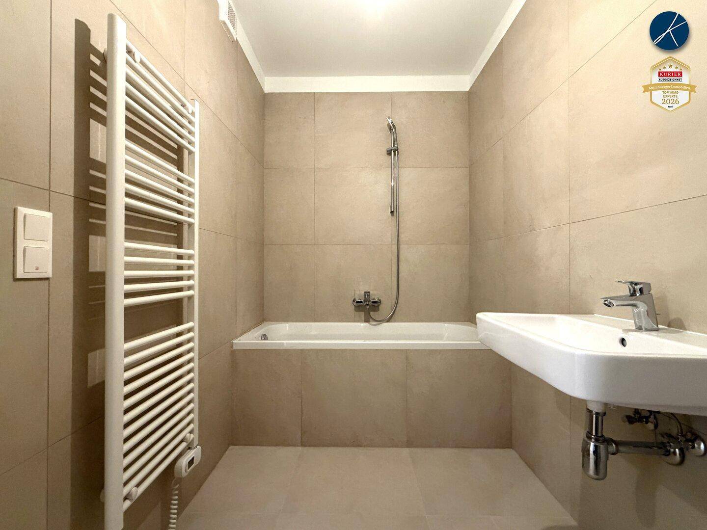 Modernes Badezimmer mit beigefarbenen Fliesen, Badewanne und beheiztem Handtuchhalter.