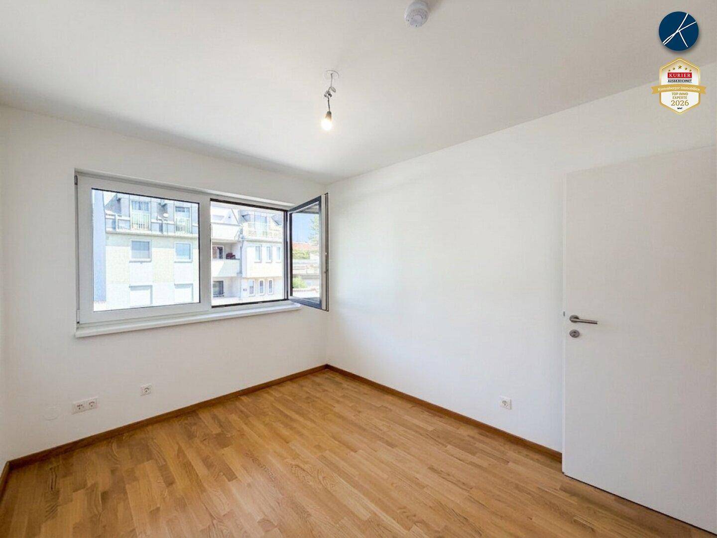 Helles Schlafzimmer mit Holzparkett und großem Fenster, das viel Tageslicht hereinlässt.