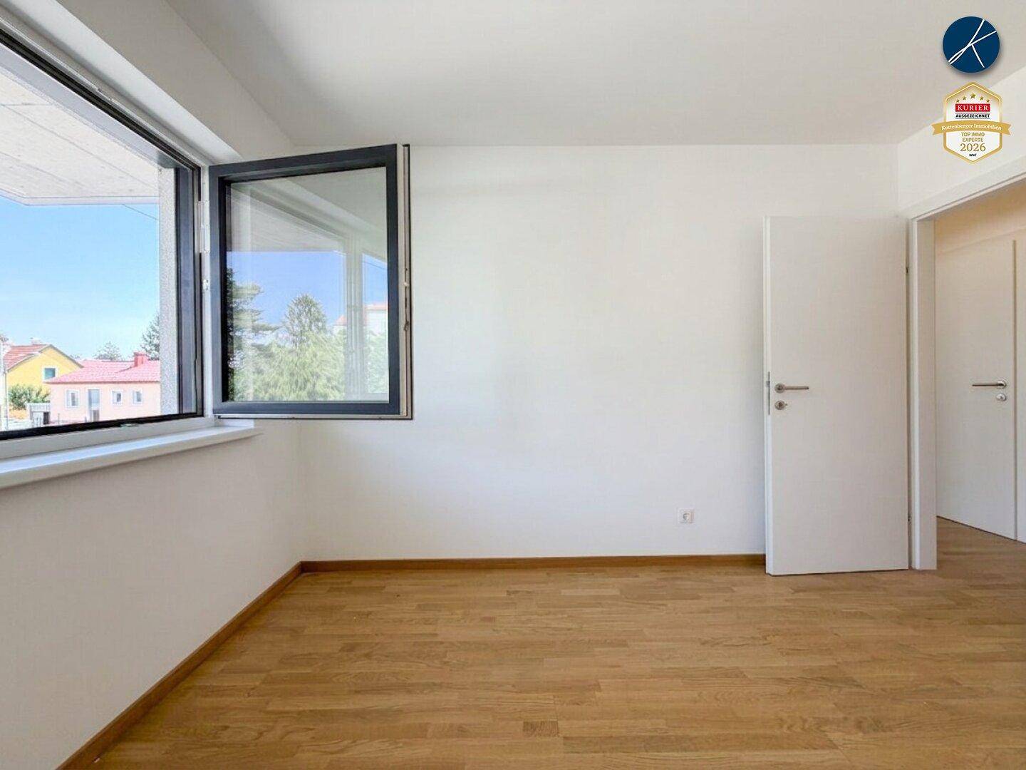 Freundliches Zimmer mit Holzparkett und Fenster, das einen weiten Blick nach draußen bietet.