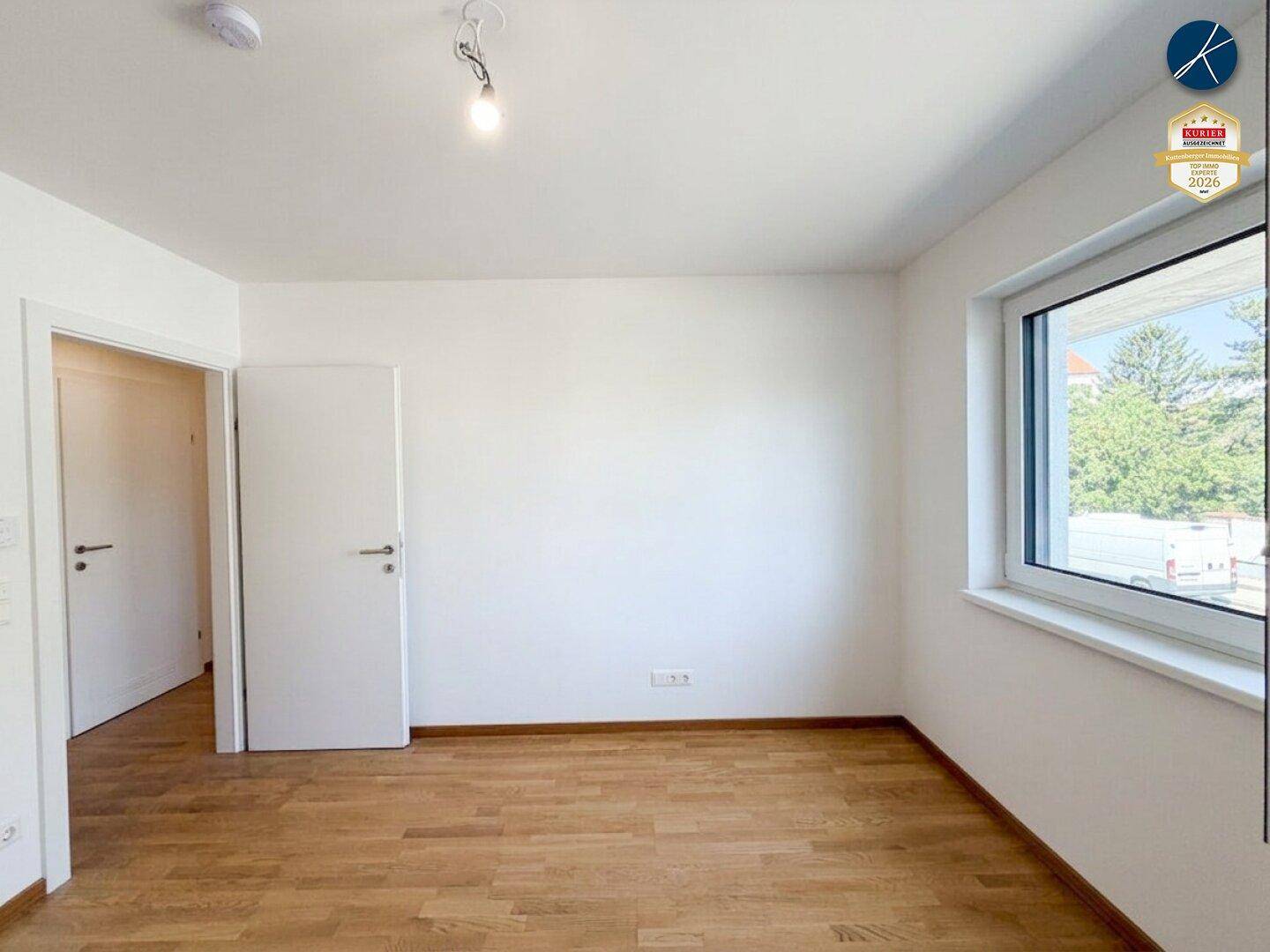 Helles Zimmer mit Holzparkett und großem Fenster, das viel Tageslicht hereinlässt.