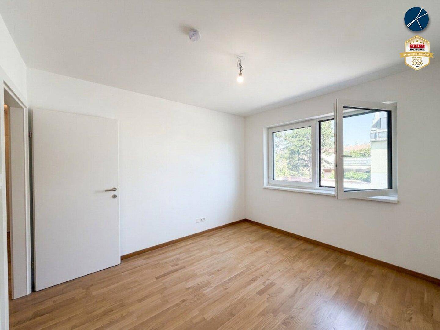 Geräumiges Zimmer mit Holzparkett und großem Fenster, das eine angenehme Wohnatmosphäre schafft.