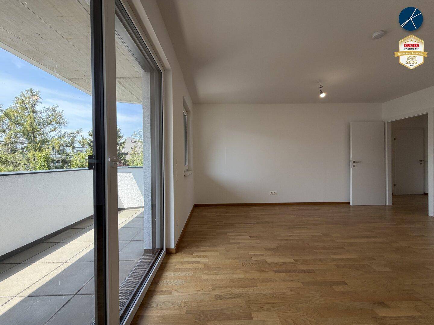 Helles, leeres Wohnzimmer mit Holzboden und großem Zugang zum Balkon, bereit zur Einrichtung.