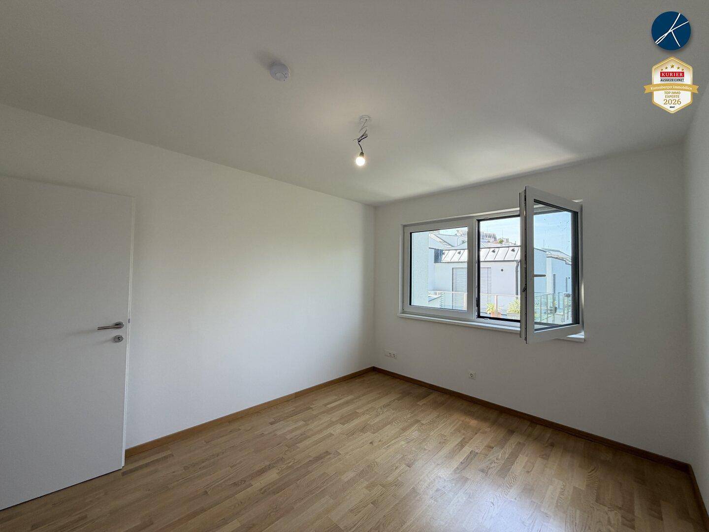 Helles Zimmer mit Parkettboden und großem Fenster, das viel Tageslicht hereinlässt.