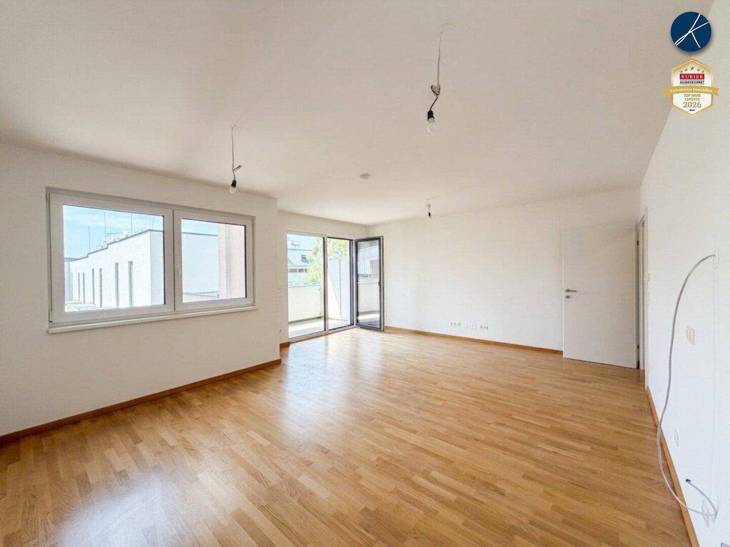 Helles, leeres Wohnzimmer mit Holzparkettboden und großen Fenstern, bereit zur individuellen Gestaltung.
