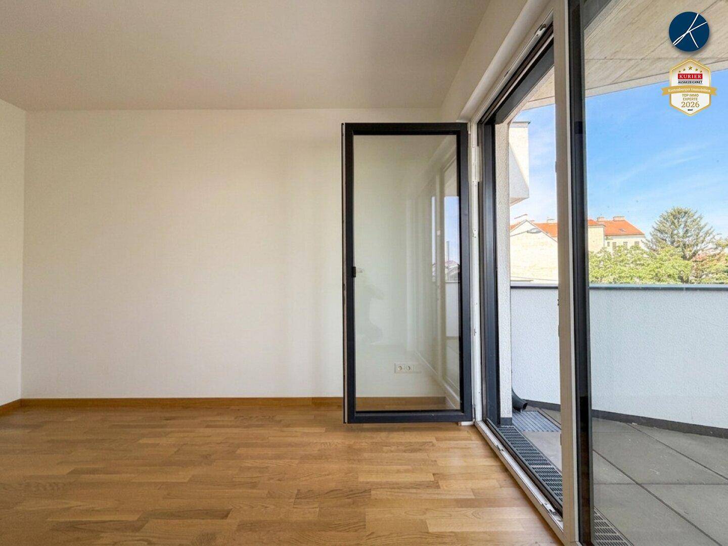 Heller Raum mit Holzparkett und Zugang zu einem Balkon, bietet viel Tageslicht.
