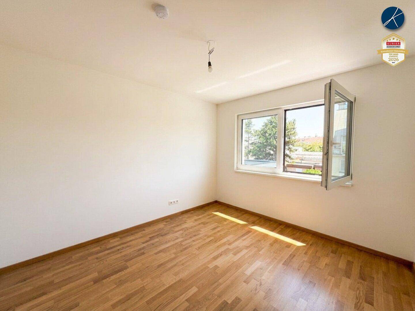 Helles Zimmer mit Holzparkett und großem Fenster, bietet viel Tageslicht und Ausblick.