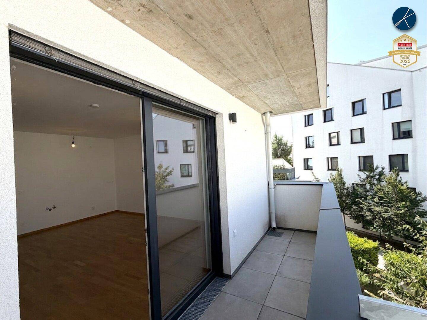 Innenansicht eines hellen Raumes mit großem Schiebefenster zum Balkon und Blick auf die Umgebung.