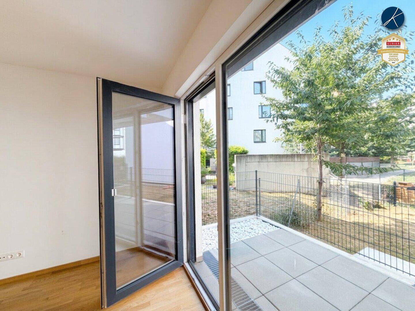 Heller Innenraum mit großen Glastüren, die auf eine kleine Außenterrasse führen.