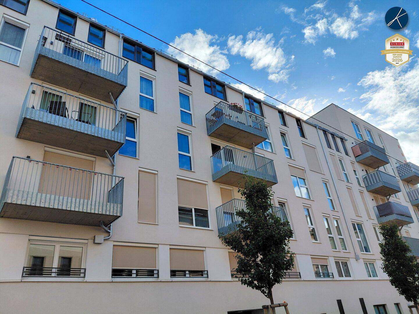 Fassade eines zeitgenössischen Wohnhauses mit vielen Balkonen und Rollläden unter blauem Himmel.