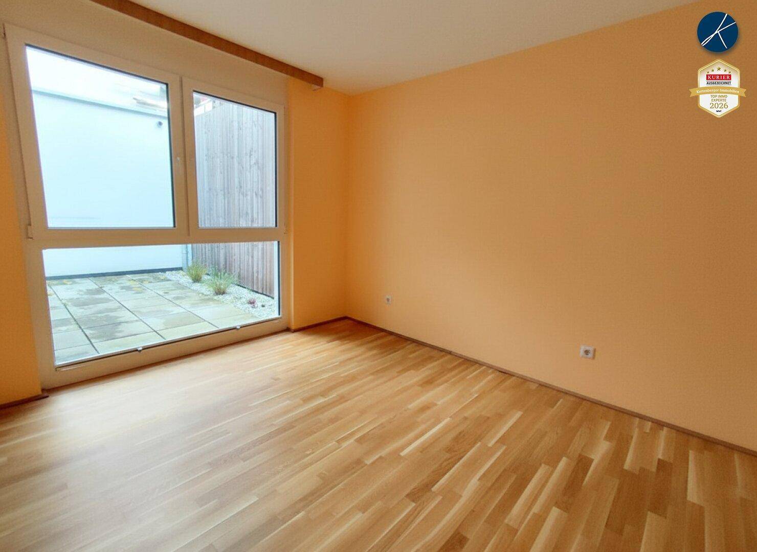 Heller Raum mit Holzparkettboden, großen Fenstern und einer Wand in warmem Orangeton.