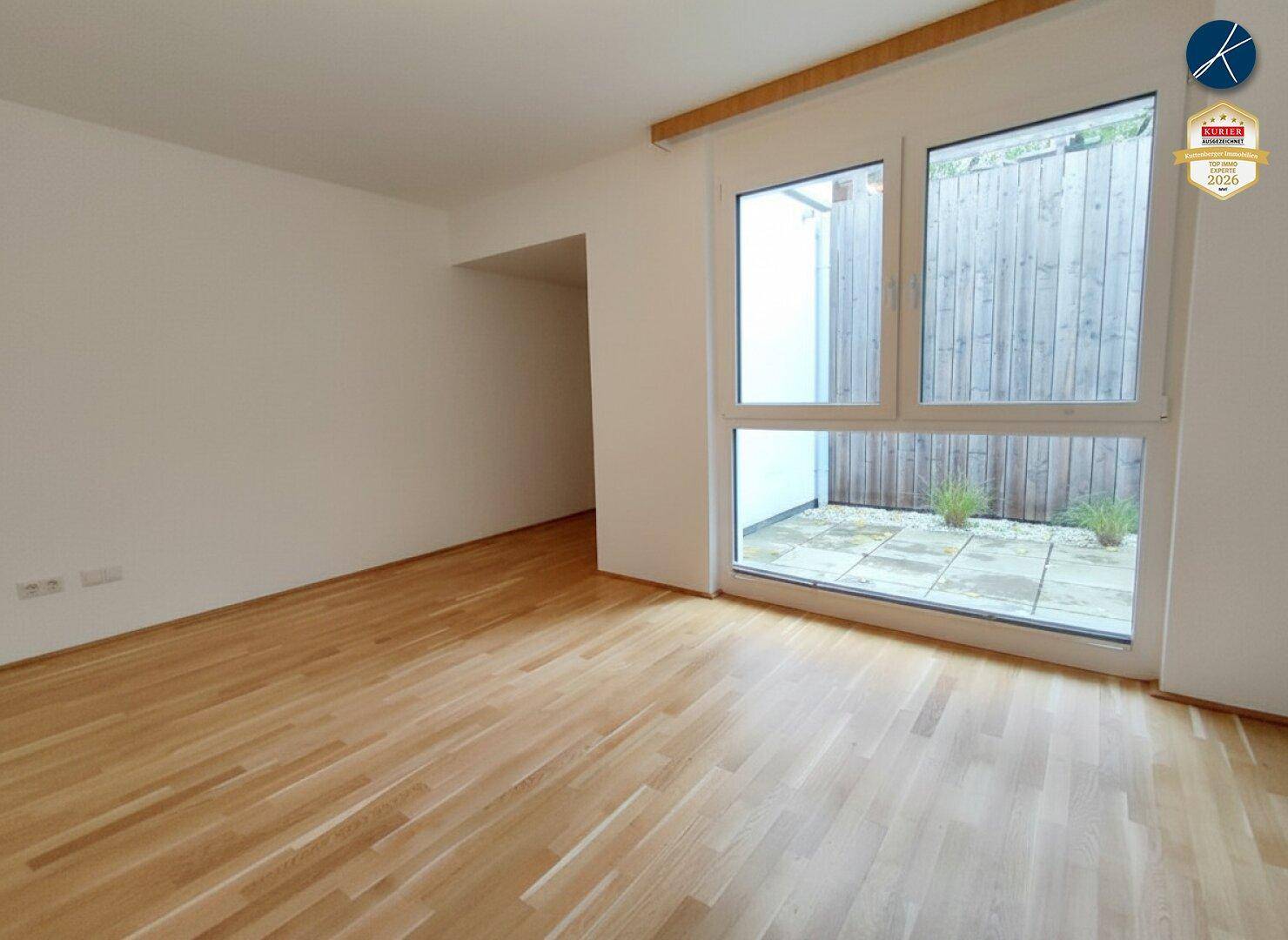 Geräumiger, heller Raum mit Holzparkettboden und großen Fenstern, die einen Blick nach draußen bieten.