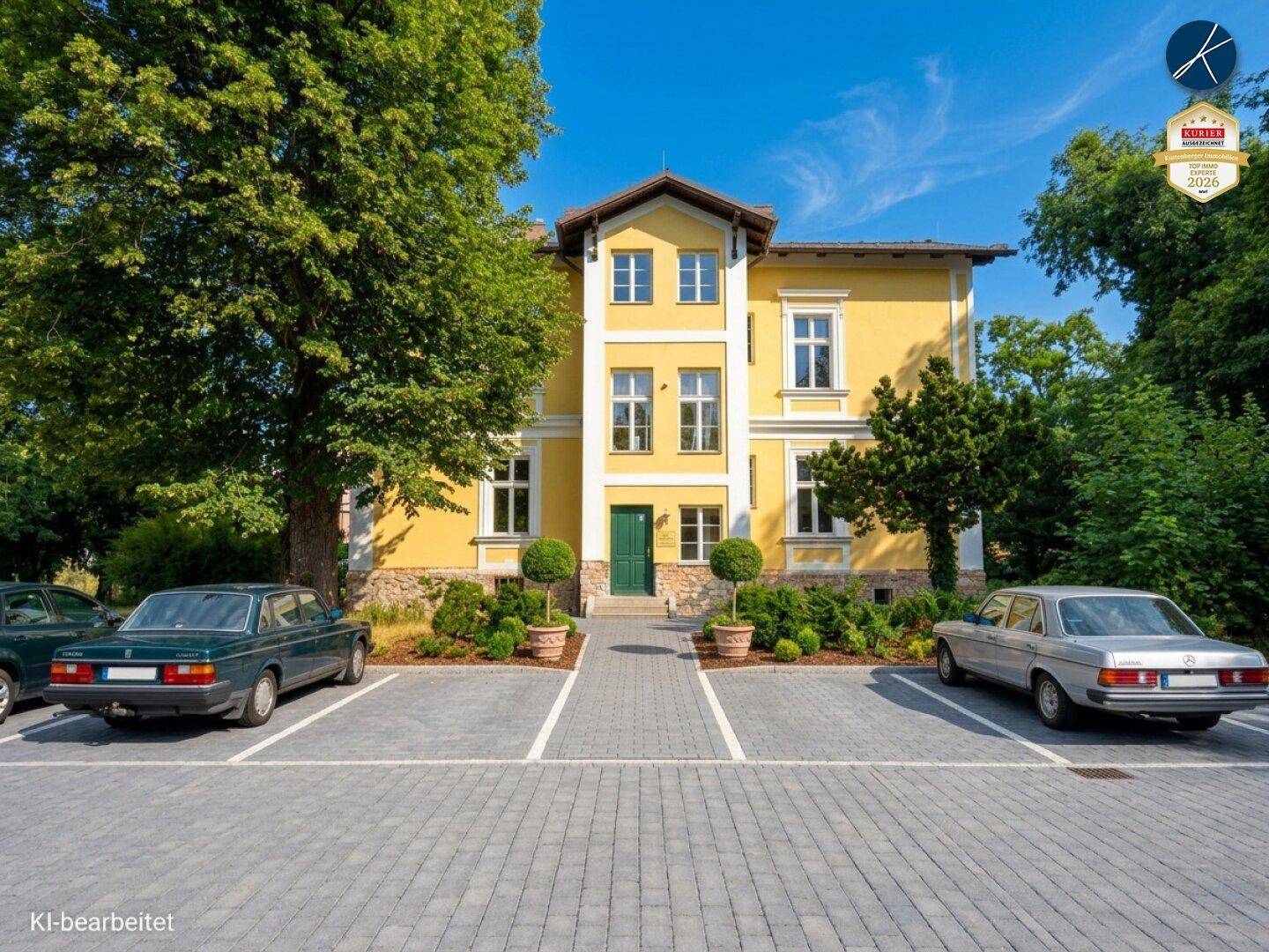 Historisches gelbes Gebäude mit gepflastertem Parkplatz und alten Autos davor unter blauem Himmel.