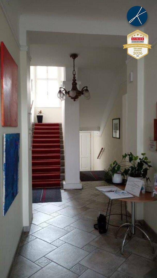 Eingangsbereich mit Fliesenboden, Treppe mit rotem Teppich und einem Kronleuchter an der Decke.