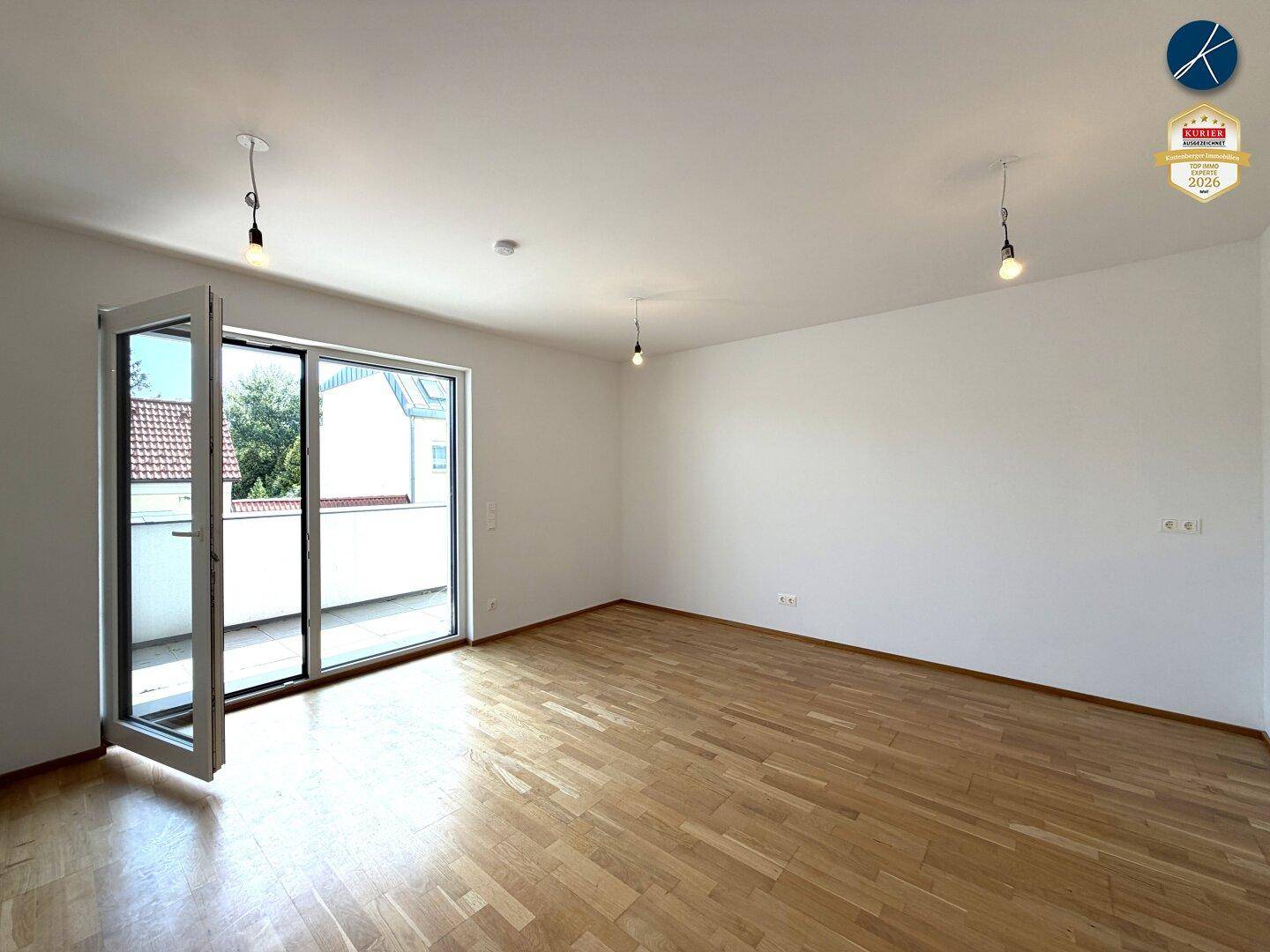 Geräumiges Wohnzimmer mit hellem Parkettboden und großen Fenstern, die viel Tageslicht hereinlassen.