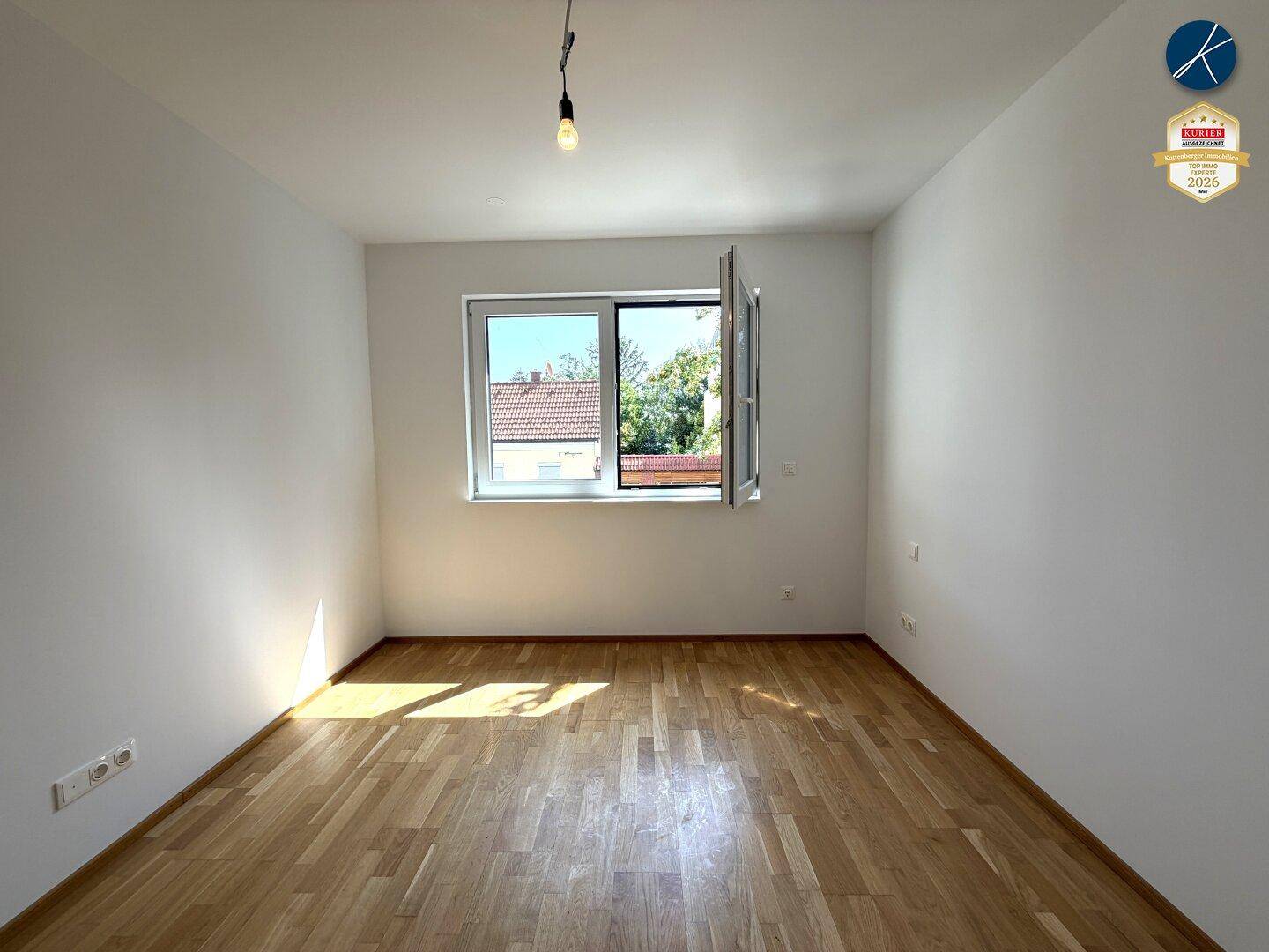 Helles Schlafzimmer mit Parkettboden und großem Fenster, das einen angenehmen Ausblick bietet.