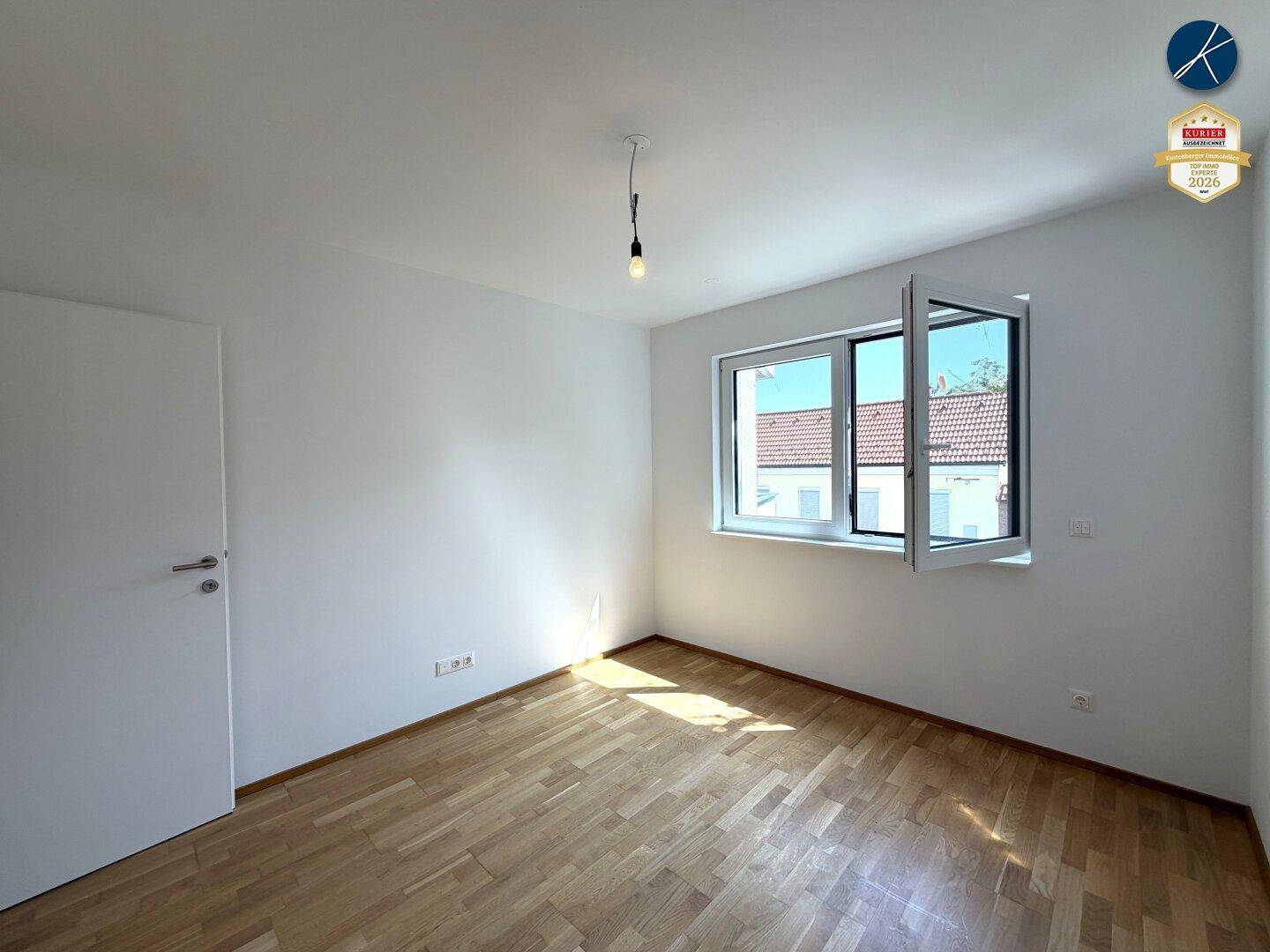 Geräumiges Schlafzimmer mit Holzboden und viel Tageslicht durch das große, weit geöffnete Fenster.