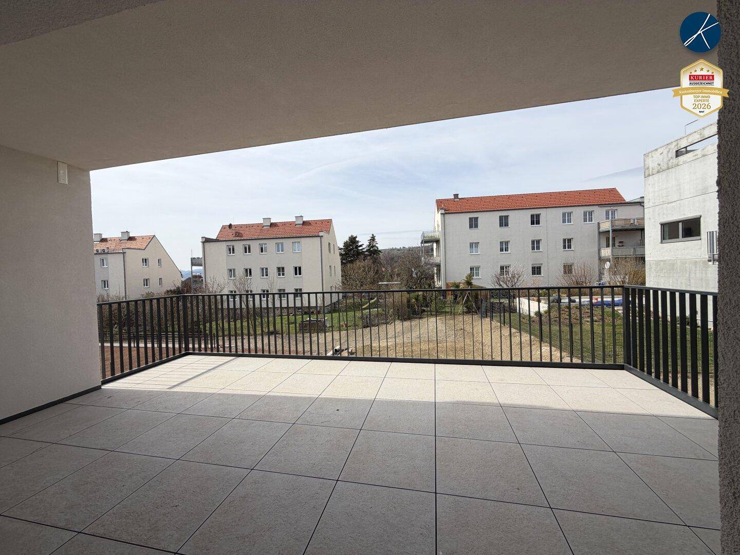Sonniger Balkon mit Fliesenboden und freiem Blick auf die umliegenden Gebäude und Grünflächen.