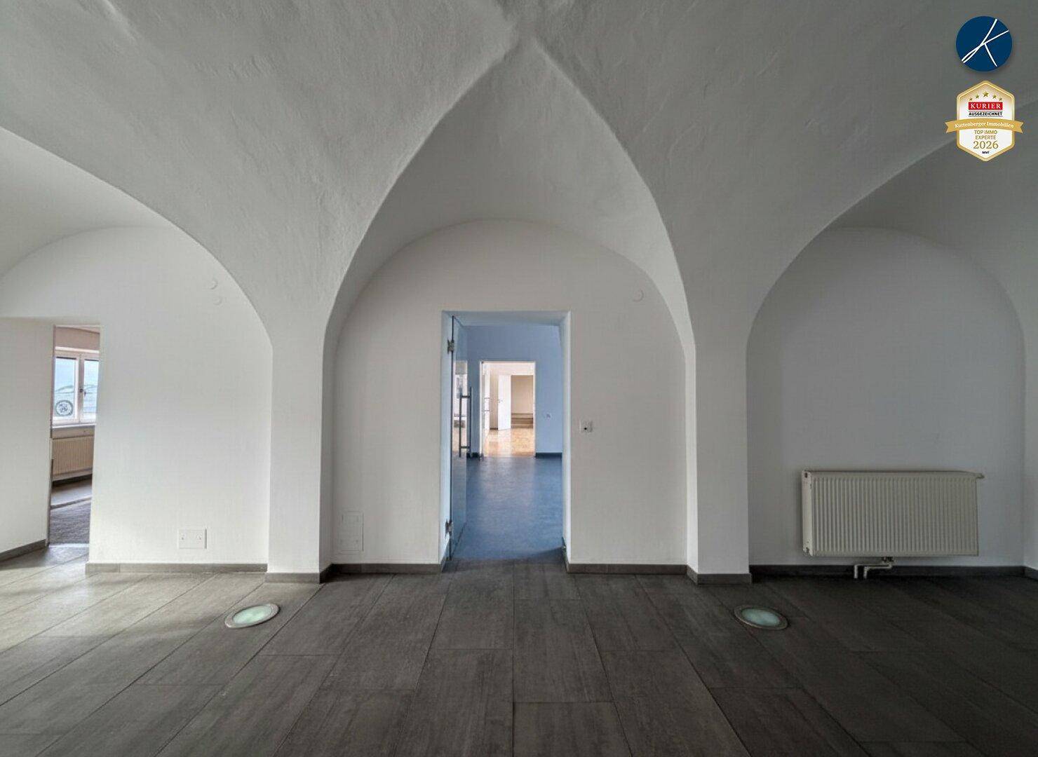 Geräumiger Raum mit eleganten Gewölbedecken und dunklem Holzboden, hell erleuchtet.