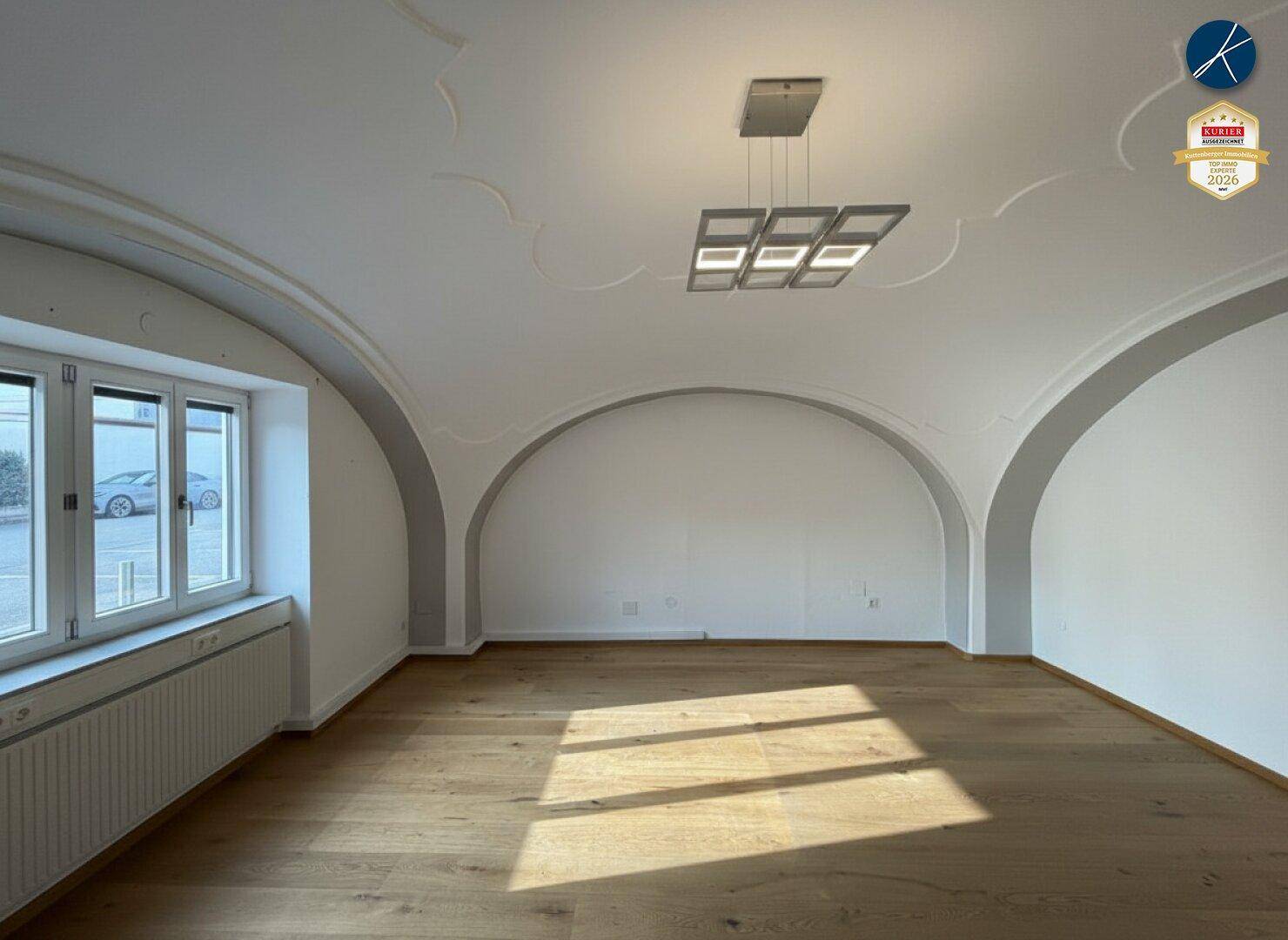 Heller Raum mit eleganten Gewölbedecken und Holzboden, durch große Fenster gut belichtet.