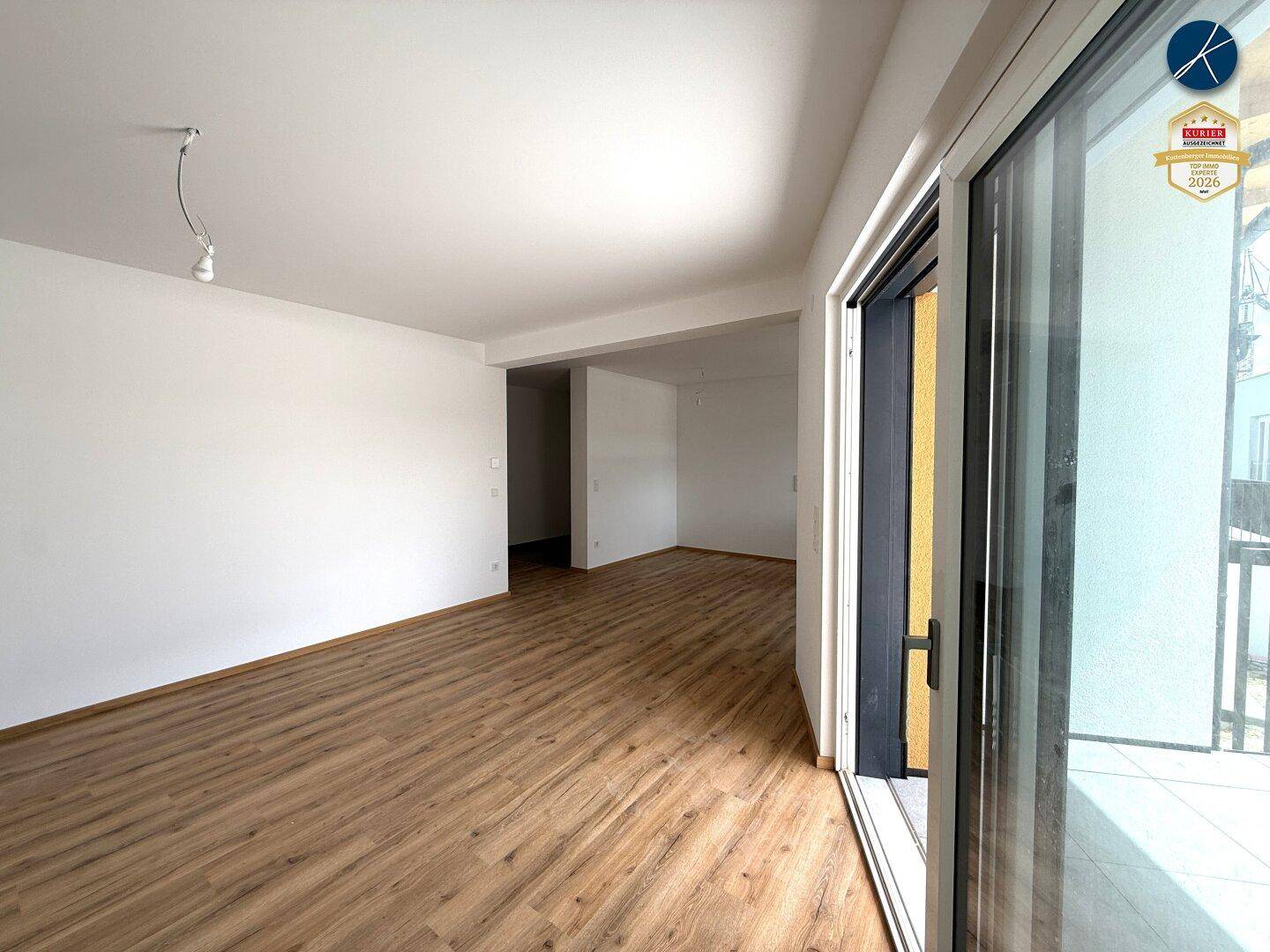 Geräumiger Wohnbereich mit hellem Laminatboden und breiter Schiebetür zur Außenterrasse.