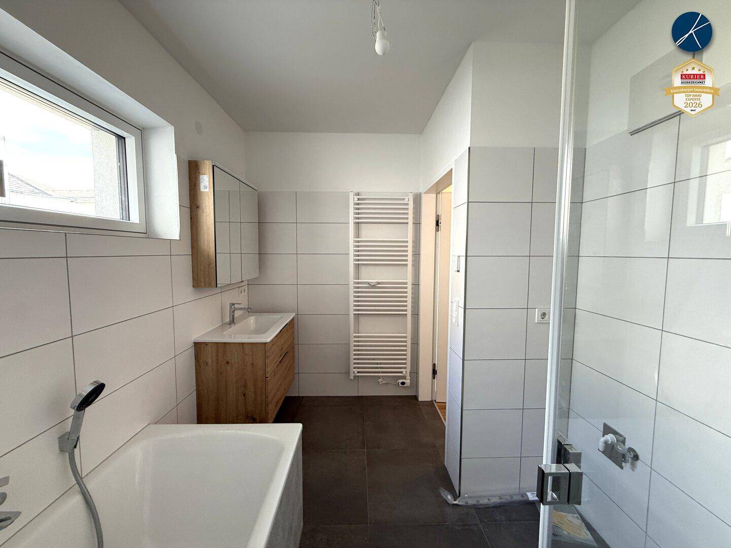 Modernes Badezimmer mit Badewanne, Dusche, Holzwaschtisch und Fenster für Tageslicht.
