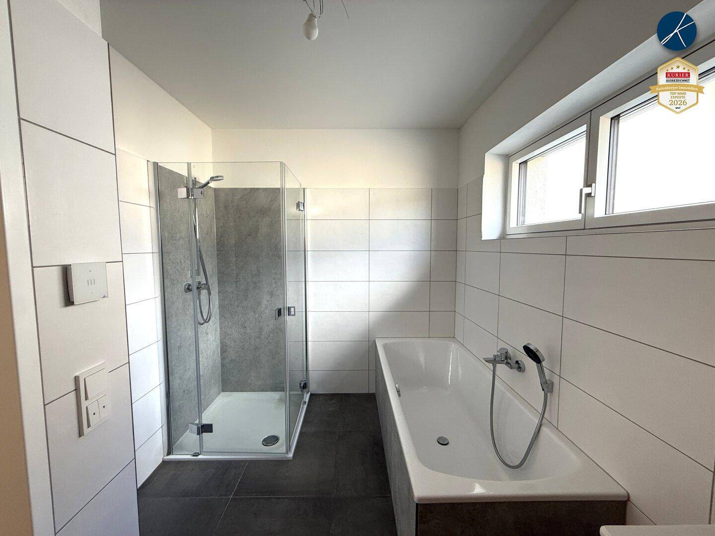 Zeitgemäßes Badezimmer mit Badewanne, Glasdusche und hellen Fliesen.