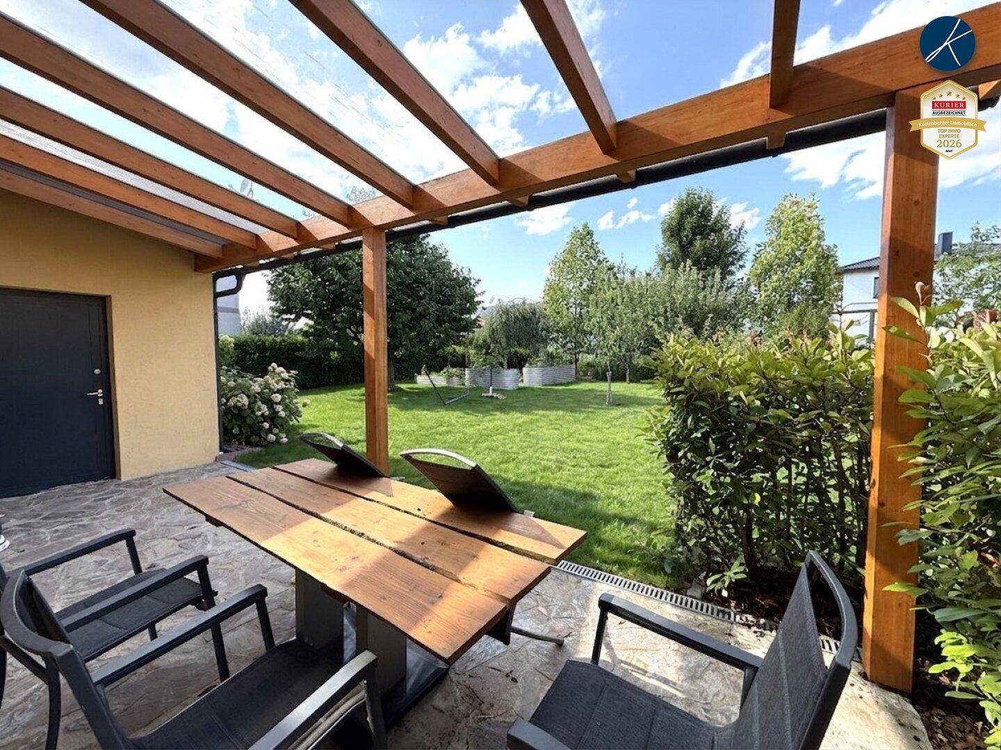 Gemütliche Terrasse mit Holzpergola und Gartenmöbeln, umgeben von viel Grün.