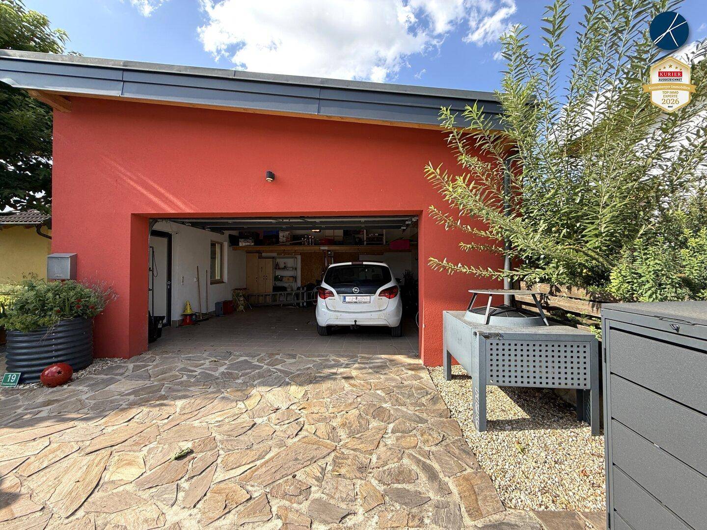 Geräumige Garage mit roter Fassade und gepflasterter Einfahrt für ein Fahrzeug.