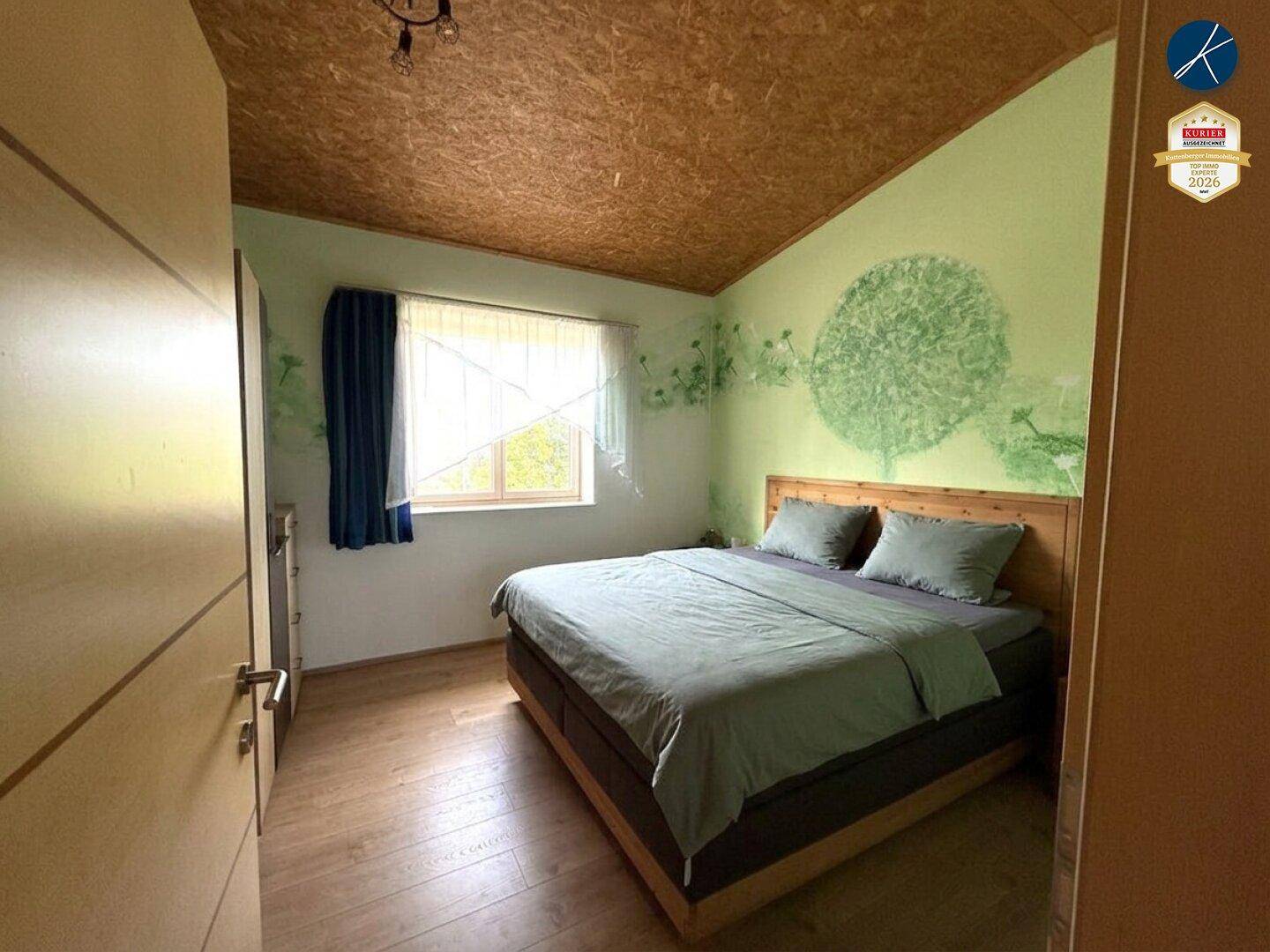 Gemütliches Schlafzimmer mit Holzbett, Holzboden und grüner Wandgestaltung.