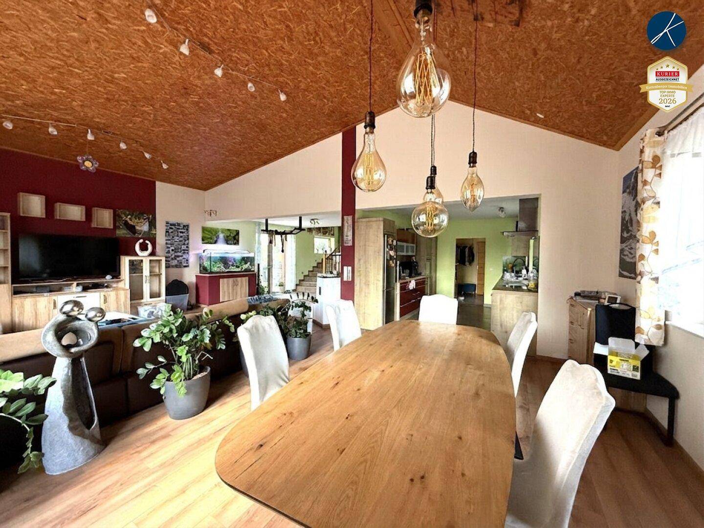 Essbereich mit großem Holztisch, modernen Hängelampen und Blick in den Wohnbereich.