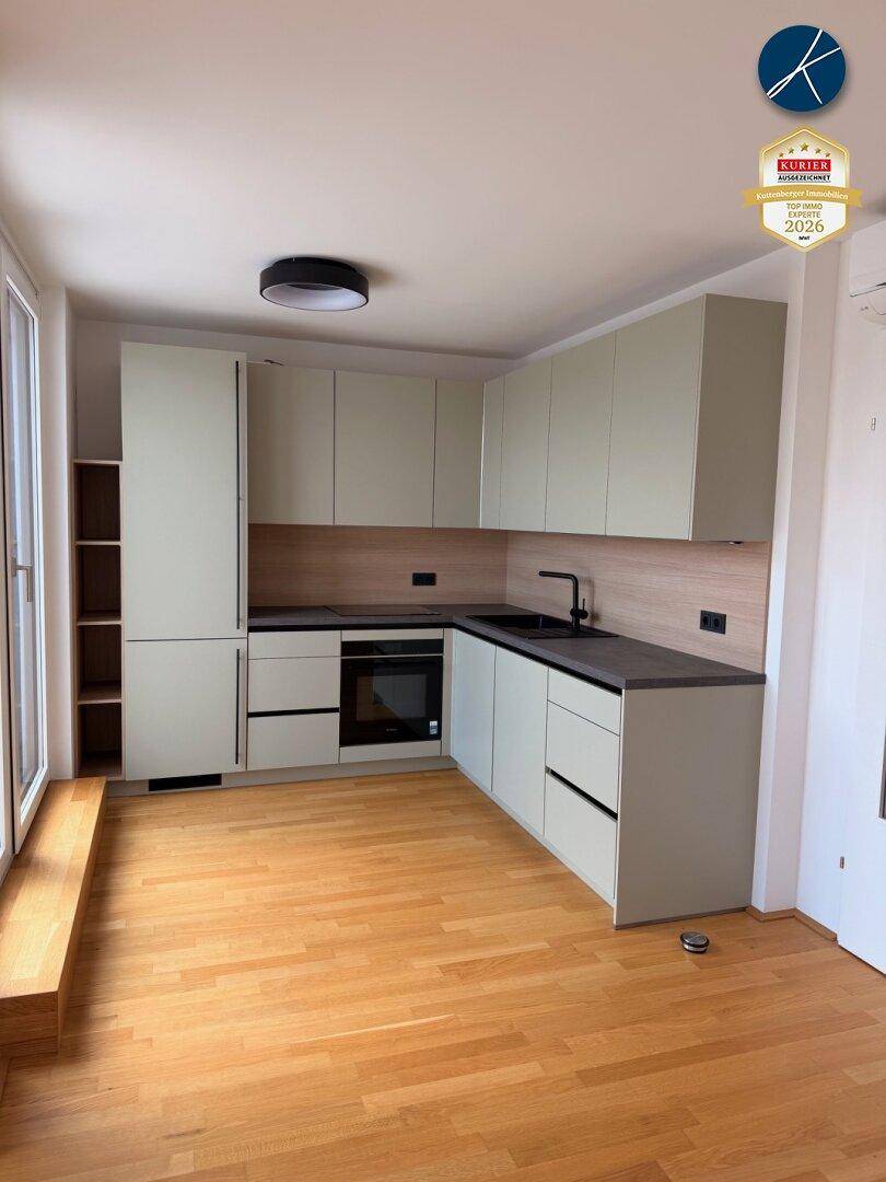 Moderne Einbauküche mit hellgrünen Schränken, dunkler Arbeitsplatte und Holzboden.