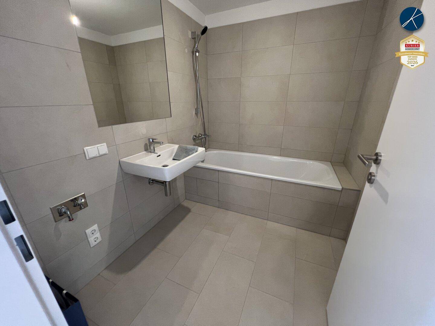 Modernes Badezimmer mit hellgrauen Fliesen, Badewanne mit Duschfunktion und Waschbecken.