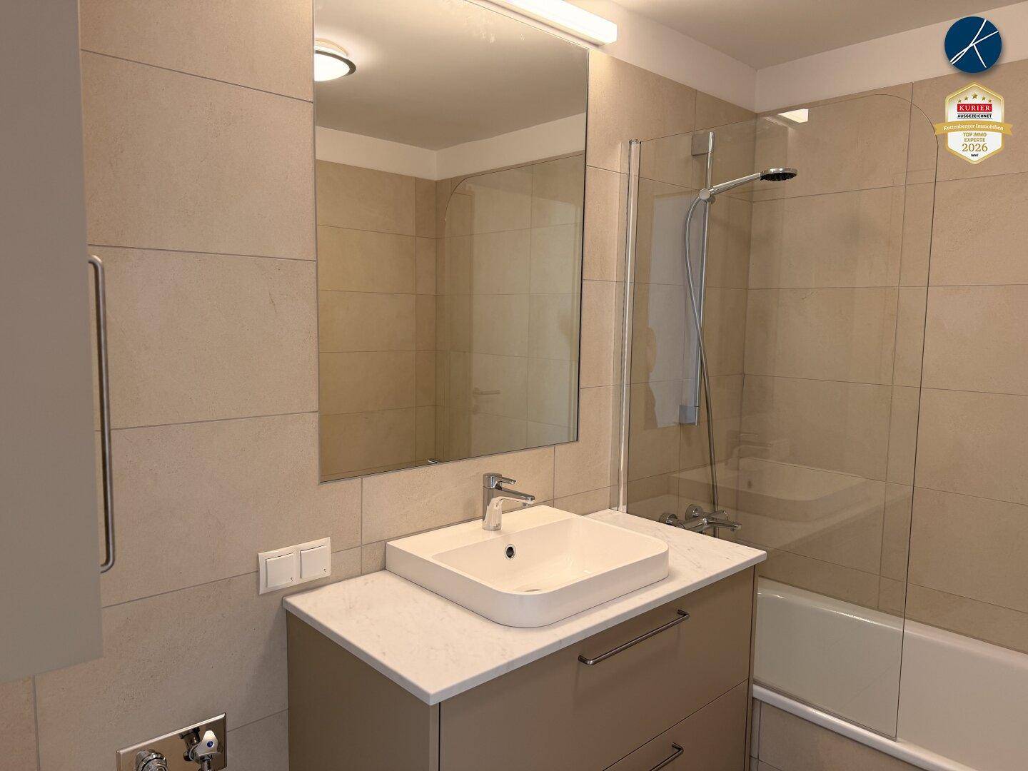 Modernes Badezimmer mit Waschtisch, großem Spiegel und Badewanne mit Duschabtrennung.