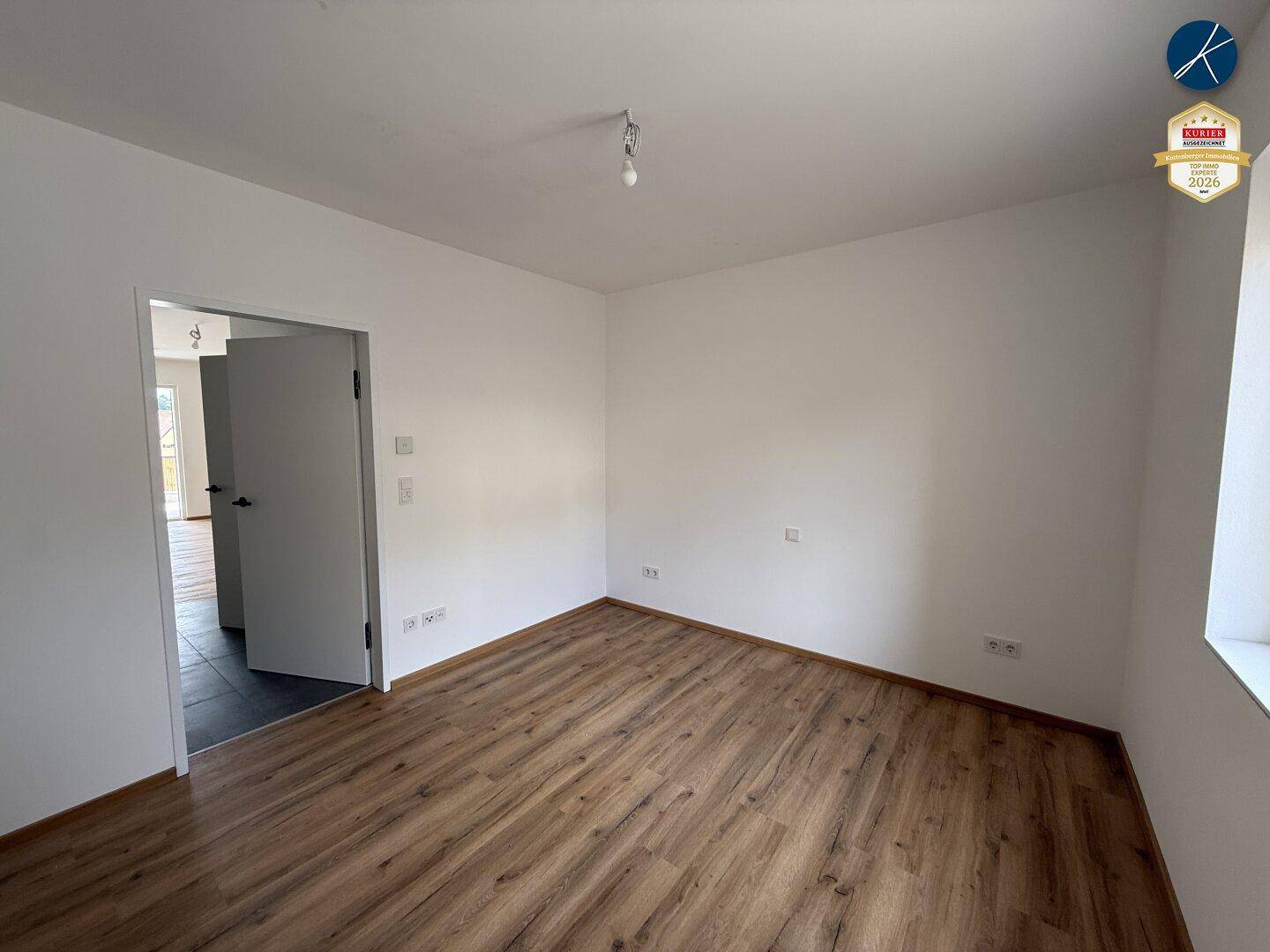 Leeres Zimmer mit Laminatboden und weiß gestrichenen Wänden, bereit zur individuellen Gestaltung.
