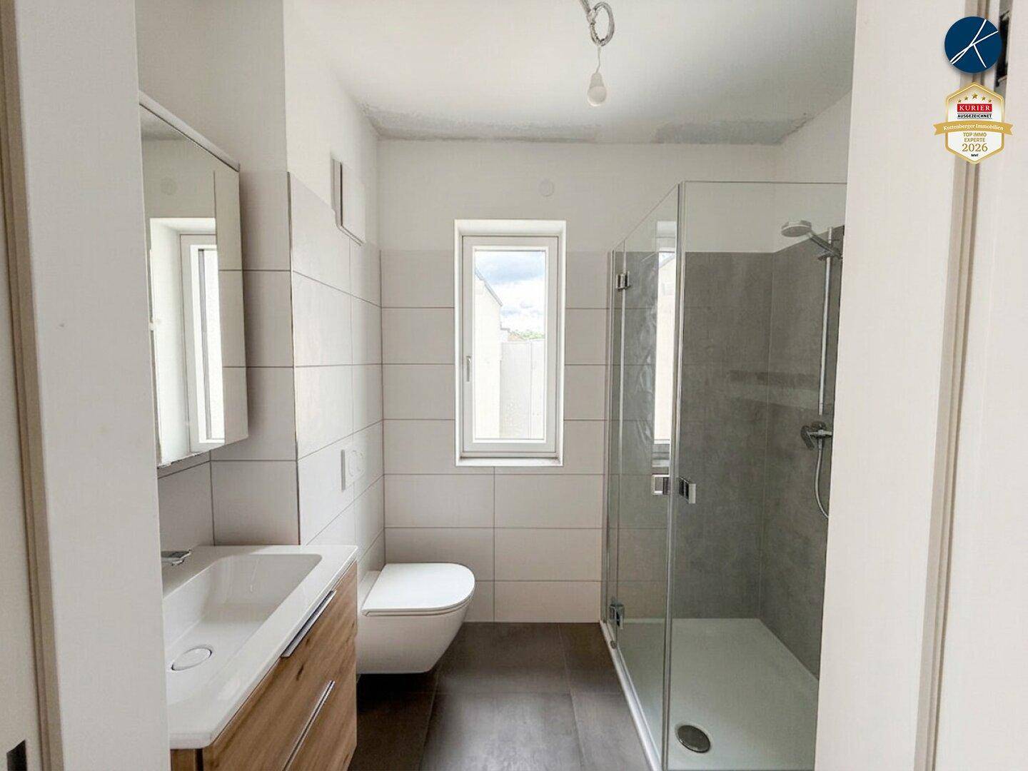 Modernes Badezimmer mit Dusche, WC, Waschbecken und Fenster für Tageslicht.