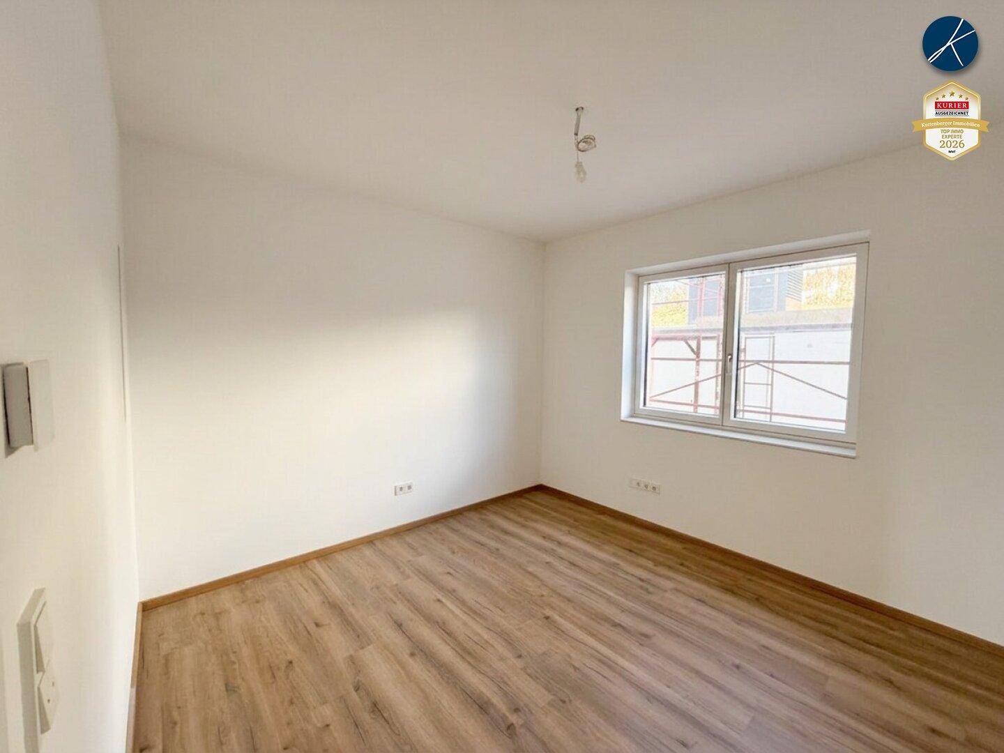Helles Schlafzimmer mit Laminatboden und einem Fenster, das viel natürliches Licht hereinlässt.