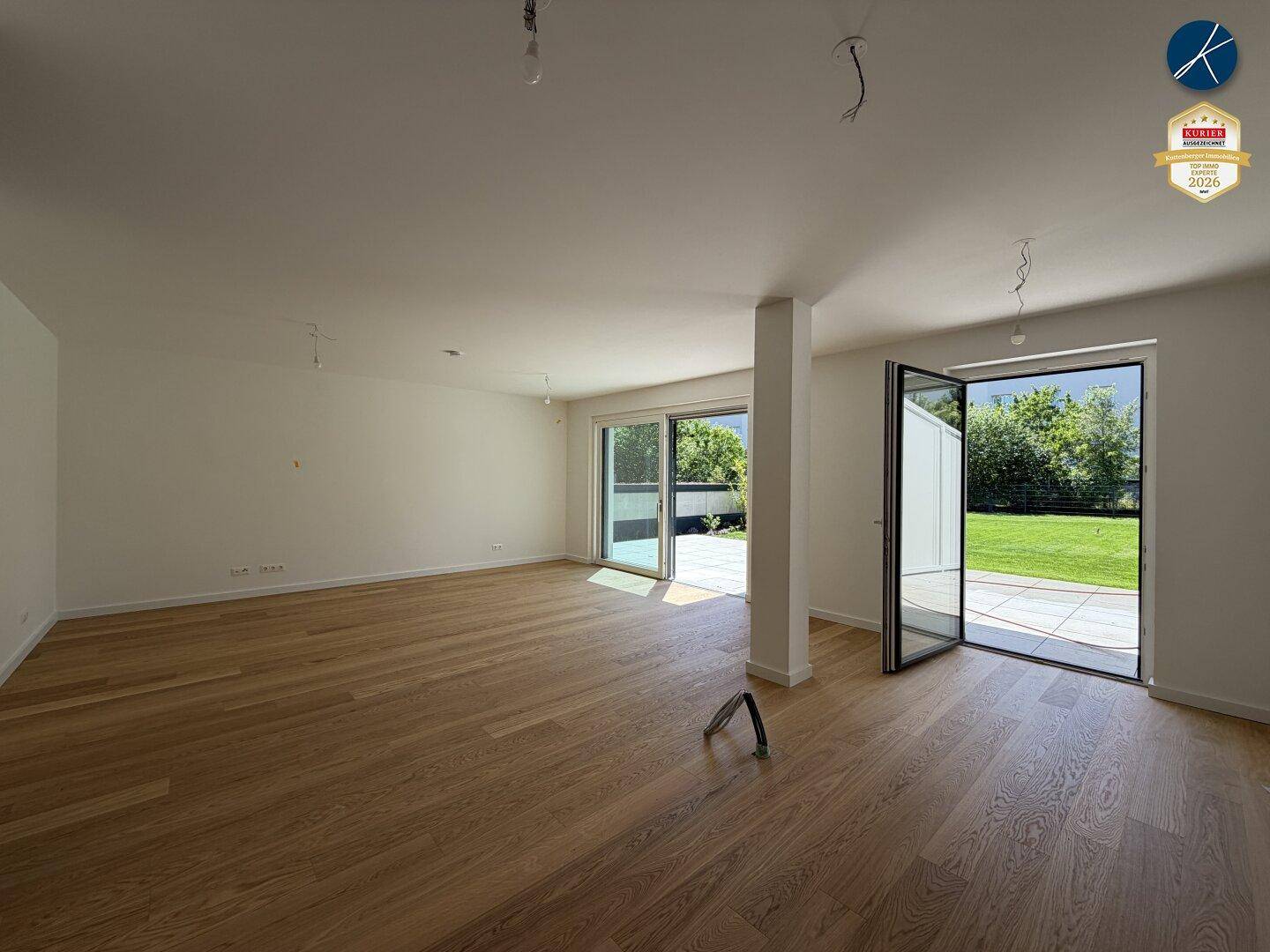Geräumiger, unmöblierter Wohnbereich mit Holzboden und Zugang zur Terrasse und Garten.