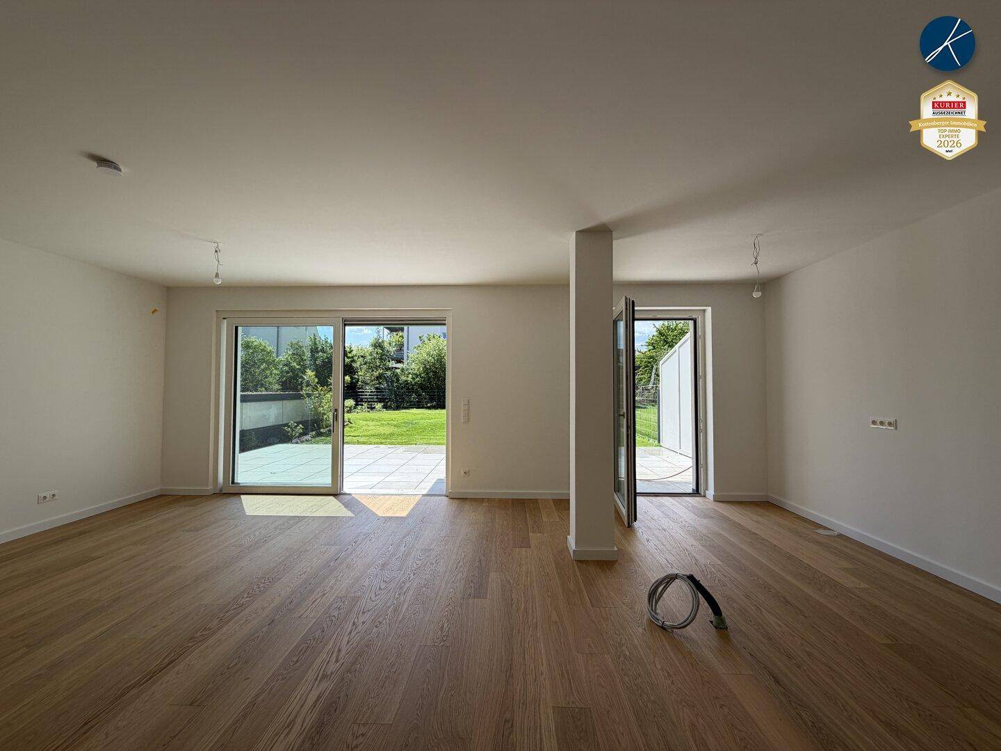 Heller Wohnbereich mit Holzboden und großen Fenstern zum Garten und zur Terrasse.