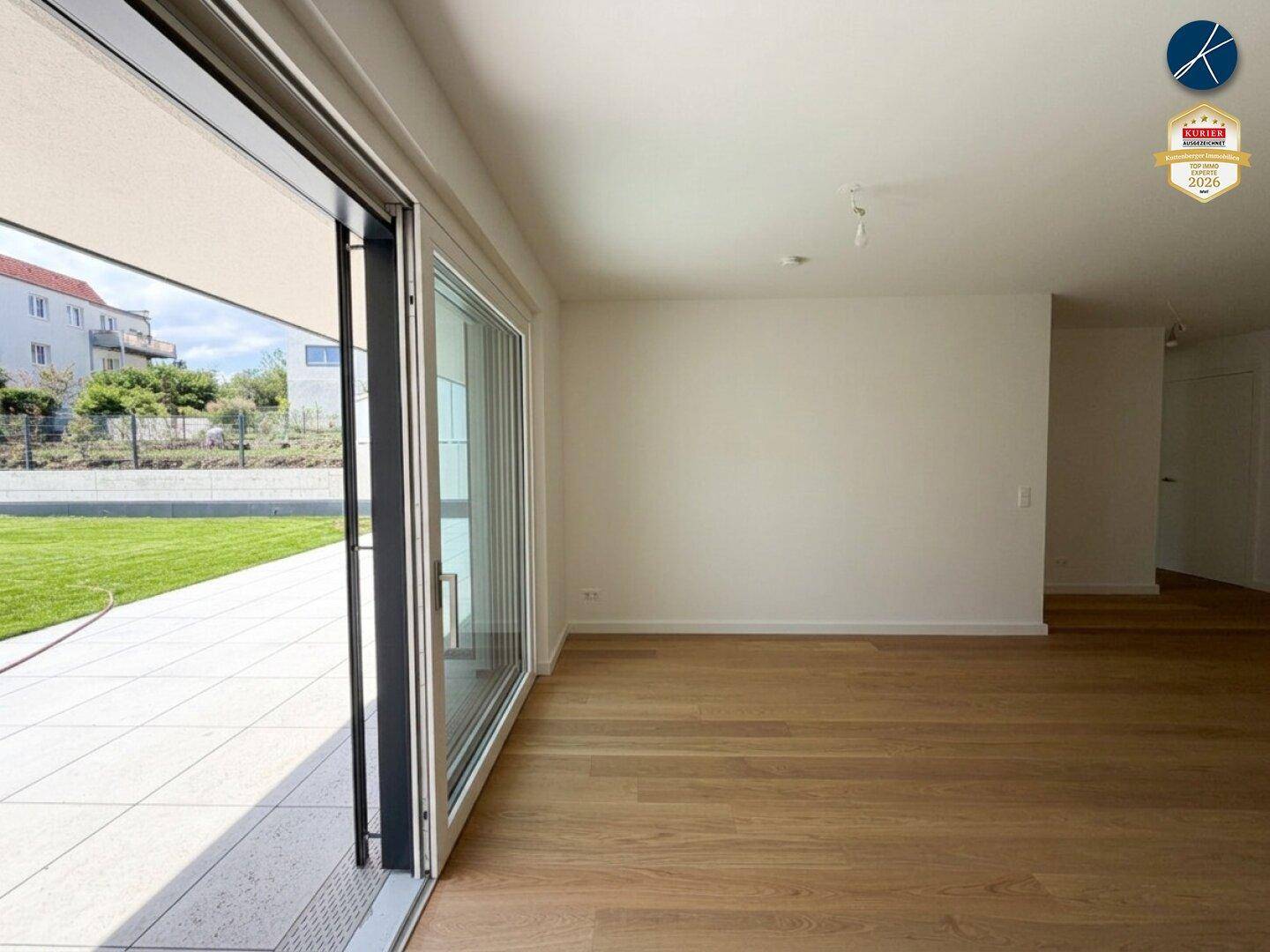 Geräumiges, leeres Wohnzimmer mit Holzboden und großen Schiebetüren, die zum Garten führen.