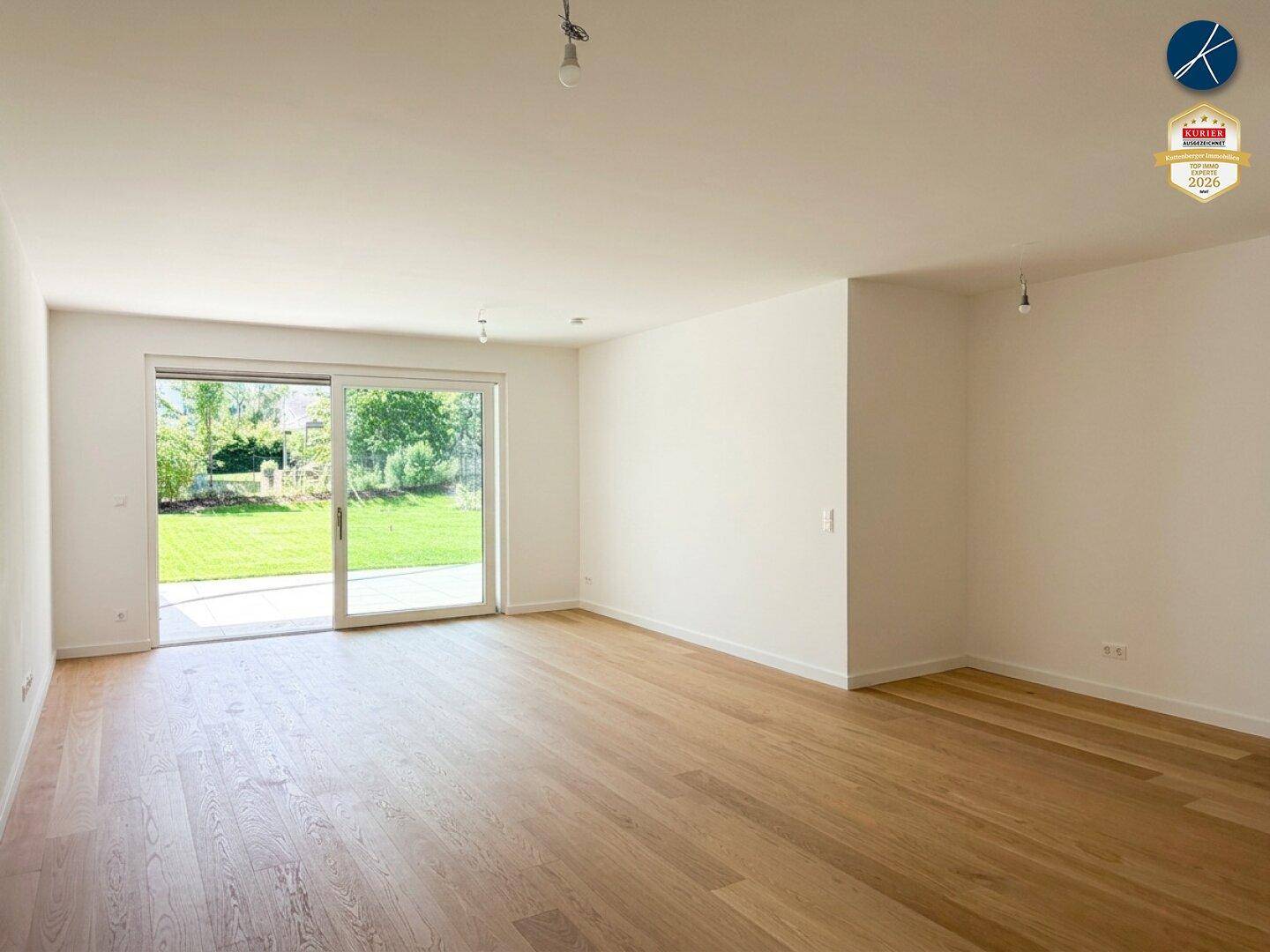 Geräumiges, leeres Wohnzimmer mit Holzboden und großen Schiebetüren zum grünen Garten.