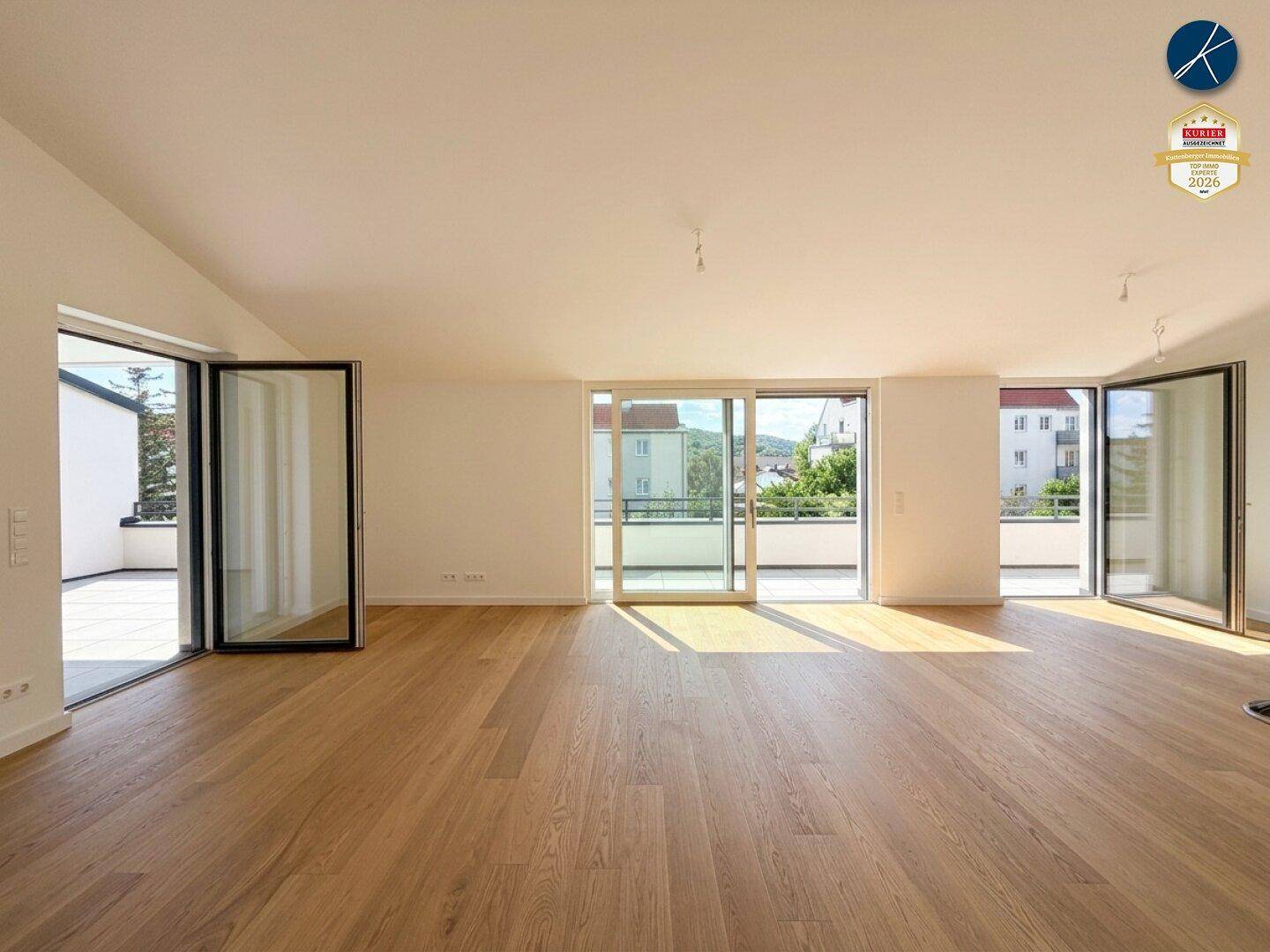 Geräumiger, leerer Wohnbereich mit großen Fensterfronten und Zugang zu mehreren Terrassen.