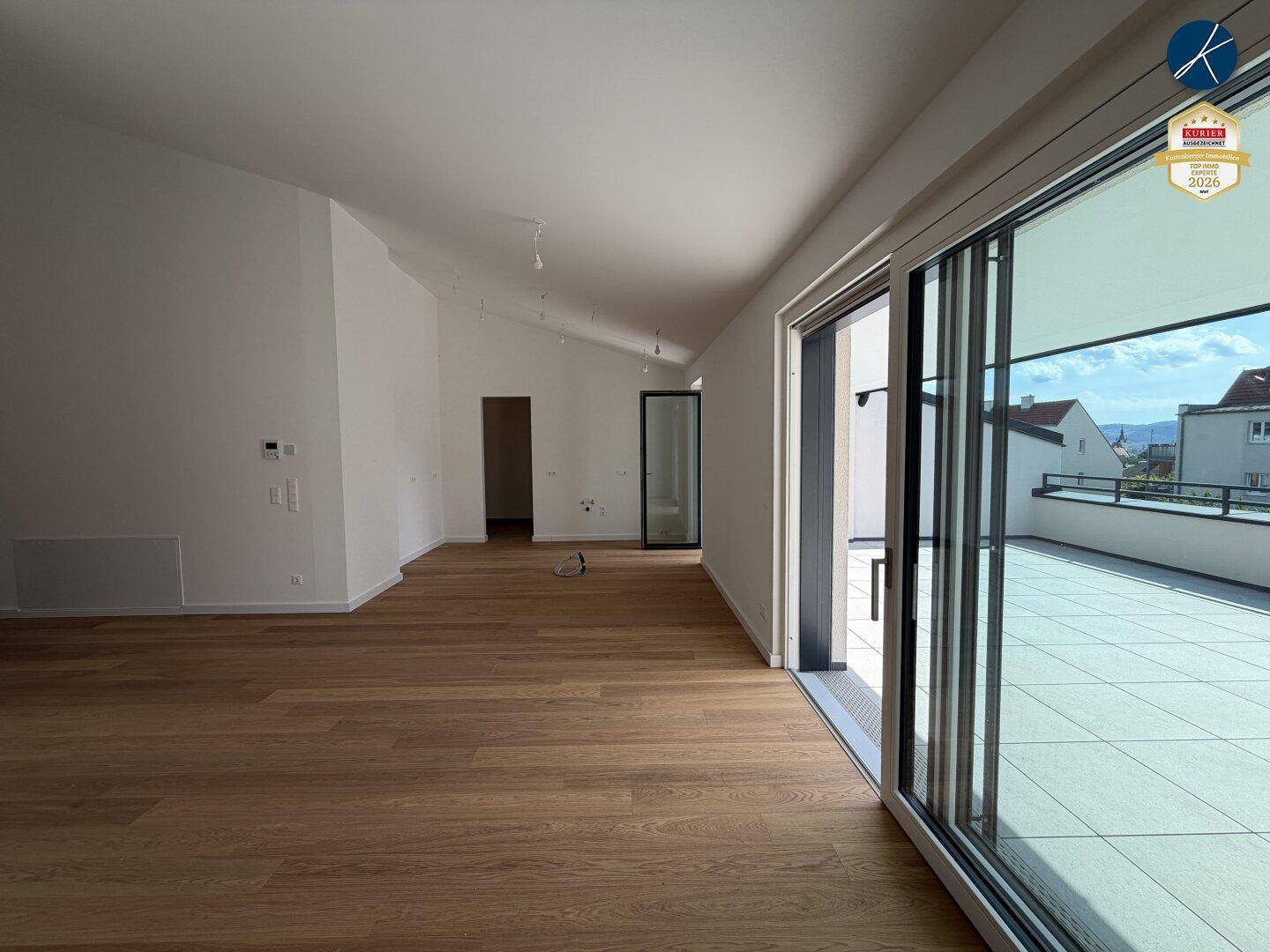 Geräumiges, leeres Wohnzimmer mit Holzboden und großen Schiebetüren, die zur Terrasse führen.
