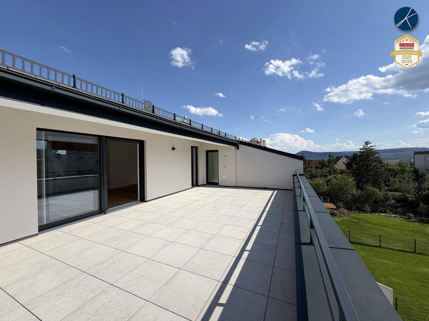 Weitläufige Dachterrasse mit Fliesenboden und Blick ins Grüne sowie auf die umliegende Landschaft.