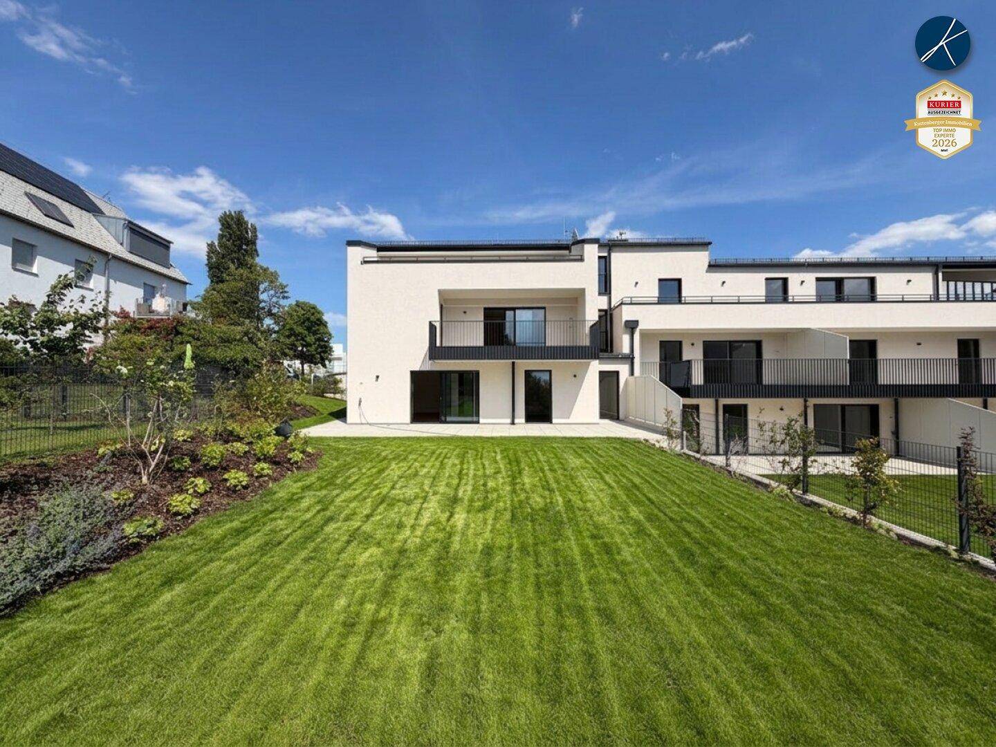 Moderne Gebäudefassade mit Balkonen und großem, grünen Gartenbereich im Vordergrund.