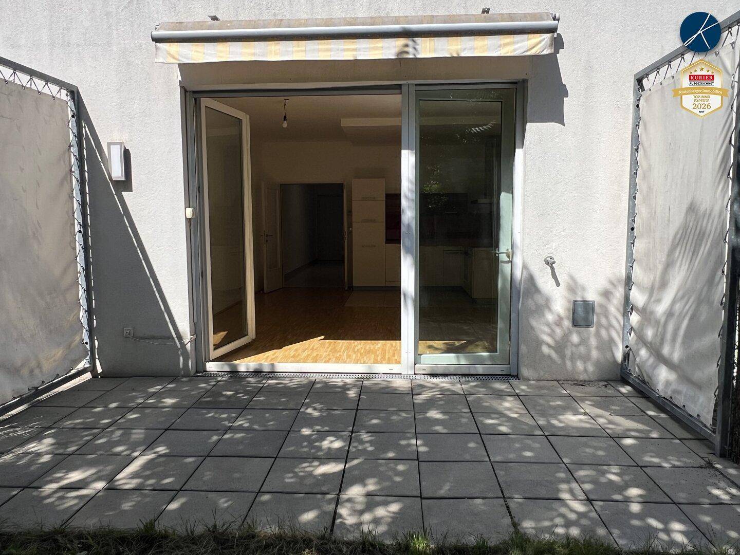Große Glasschiebetür führt von der gepflasterten Terrasse in den hellen Innenbereich.