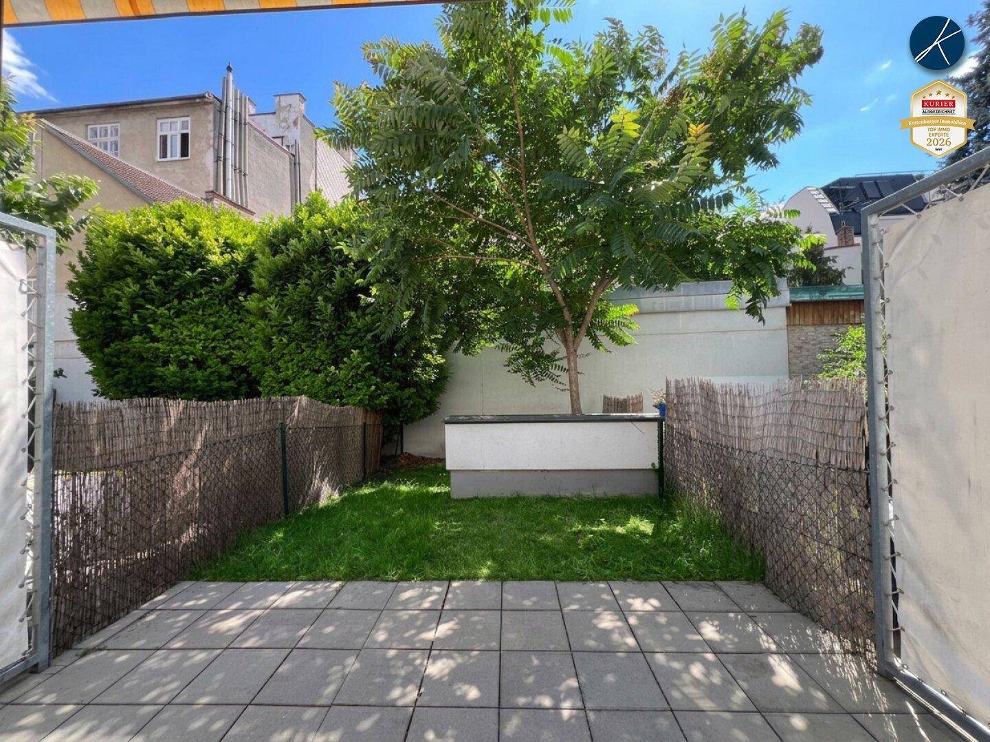 Gepflasterte Terrasse mit Zugang zu einem kleinen Gartenbereich und Blick ins Grüne.