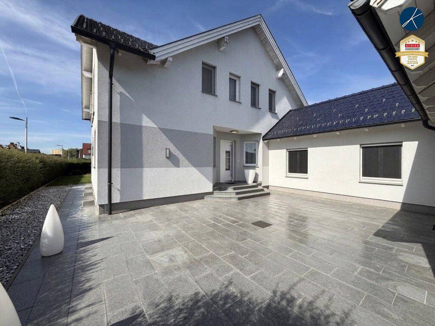 Seitenansicht des Hauses mit gepflastertem Vorplatz, Eingangsbereich und moderner Architektur.
