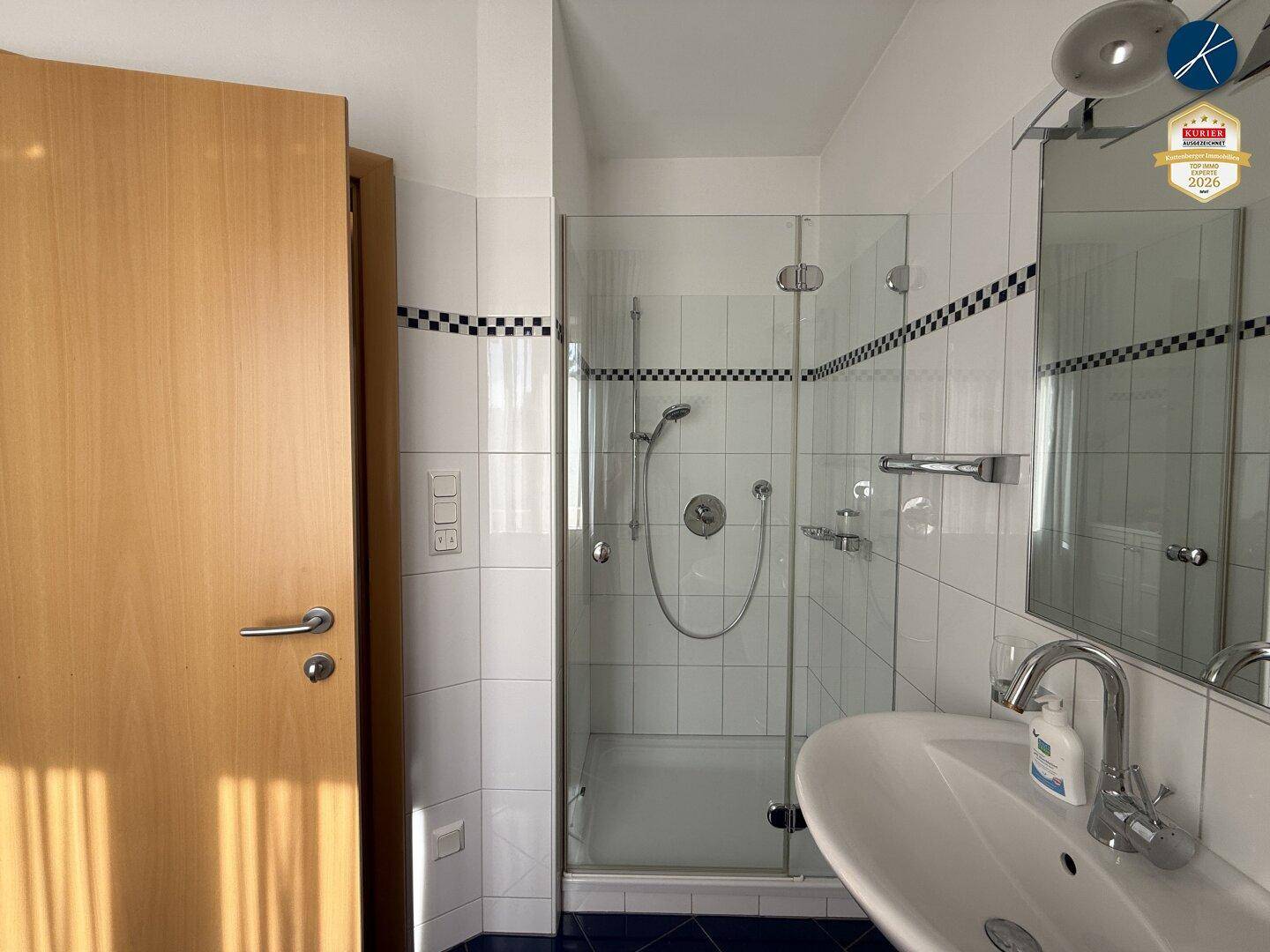 Modernes Badezimmer mit Duschkabine, Waschbecken und weißen Fliesen mit blauen Akzenten.
