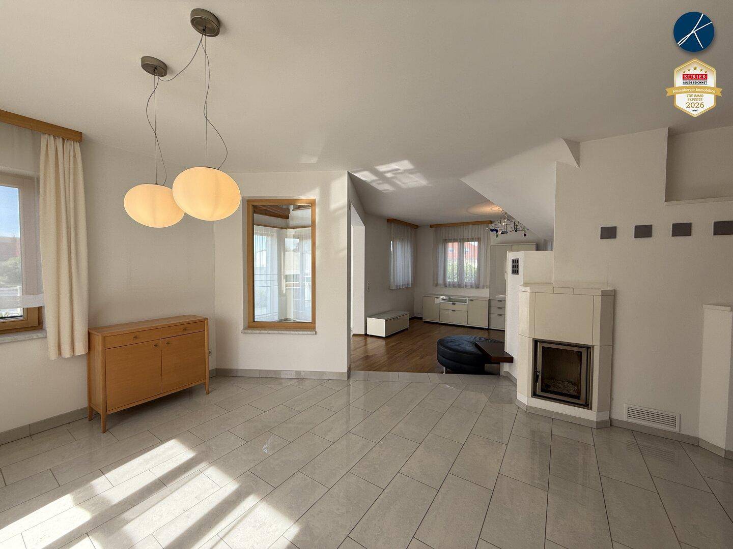 Geräumiges Wohnzimmer mit Kamin, Fliesenboden und Übergang zu einem Bereich mit Holzparkett.